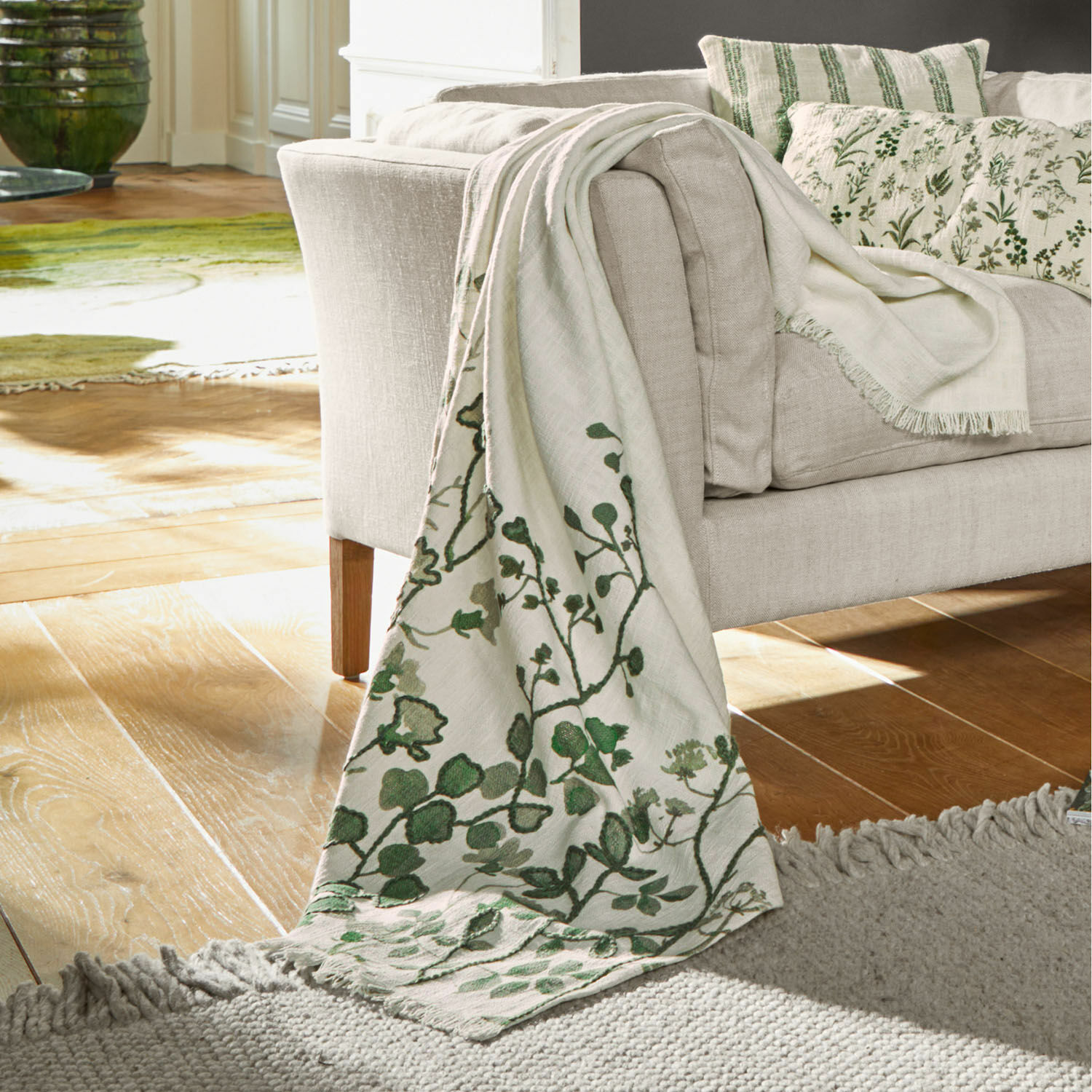 Manta beige con diseño vegetal verde sobre sofá, material suave, decoración acogedora