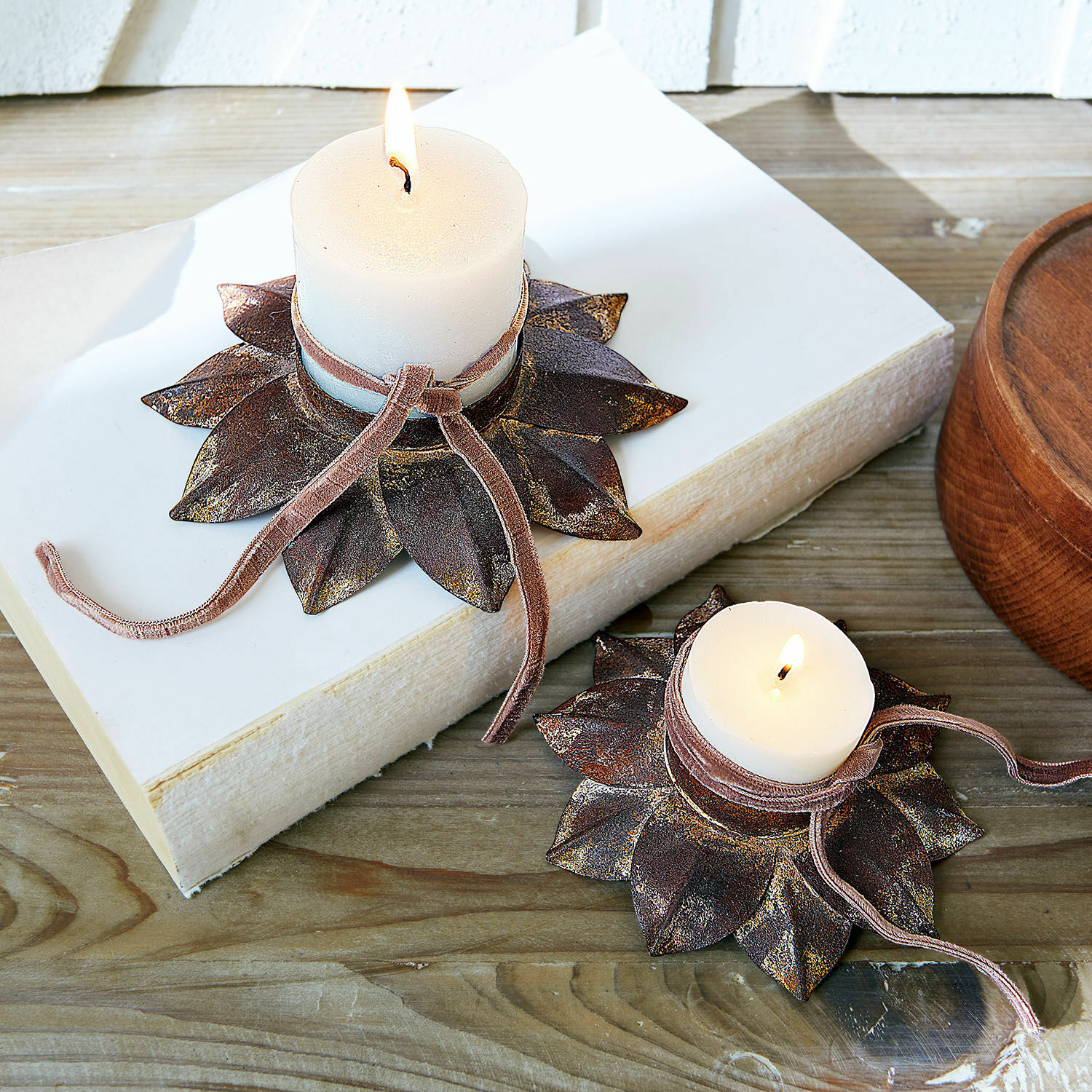 Set de 2 candeleros Viverto Portavelas metálicos con forma de hojas en acabado marrón y velas blancas sobre mesa de madera