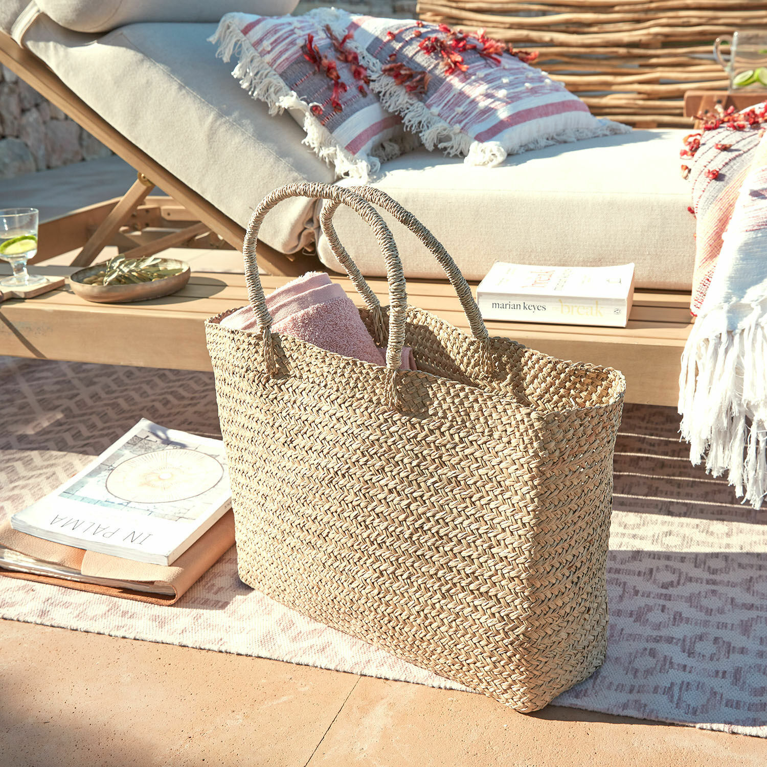 Bolso Ventresque Bolsa trenzada natural de hierba marina con toalla rosa en terraza junto a tumbona