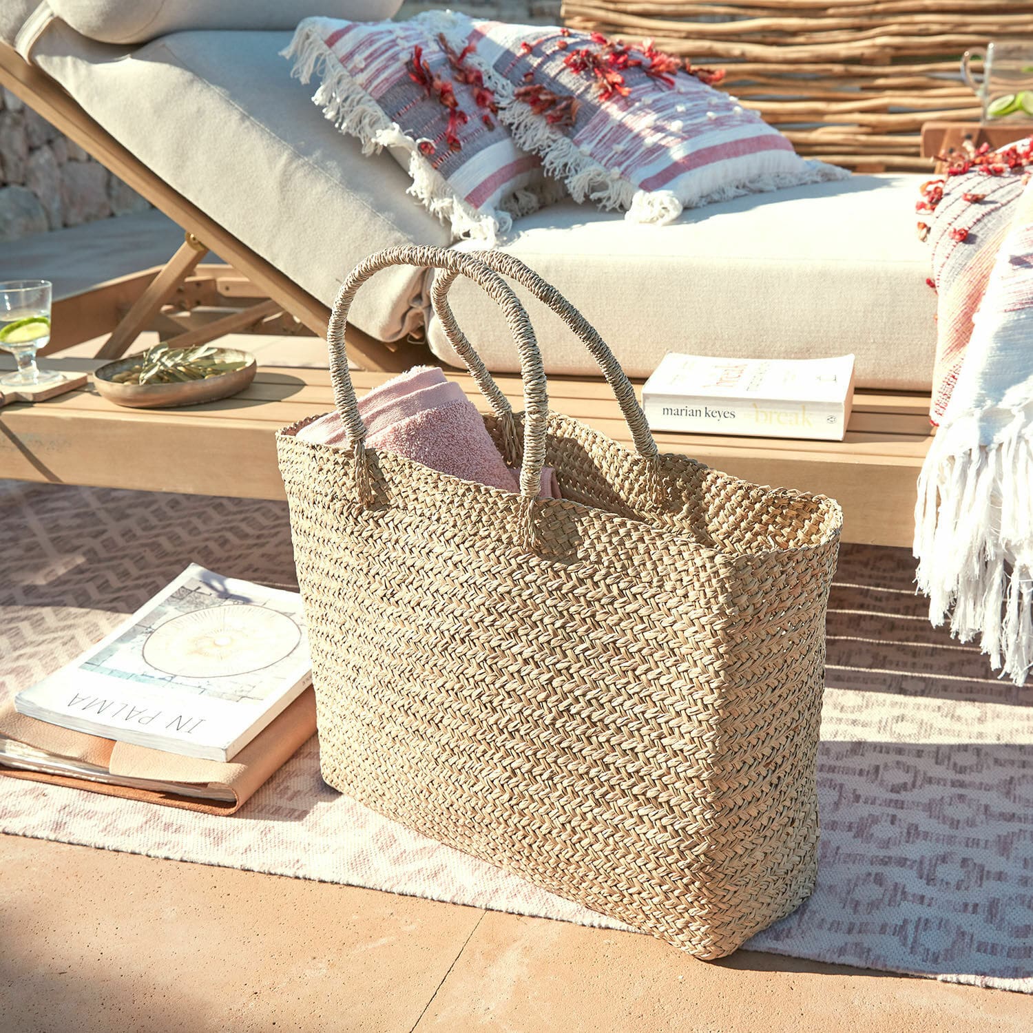 Bolso Ventresque Bolsa trenzada natural de hierba marina con toalla rosa en terraza junto a tumbona