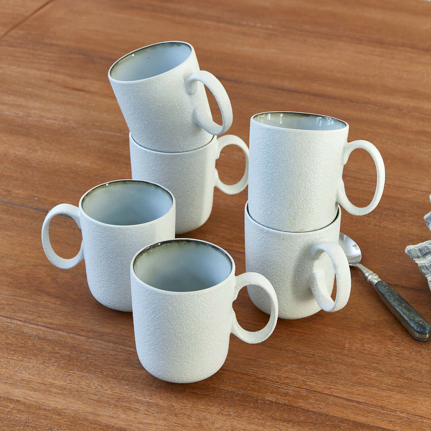 Set de 6 tazas Eiruna Conjunto de seis tazas de cerámica blanca con superficie texturizada sobre mesa de madera