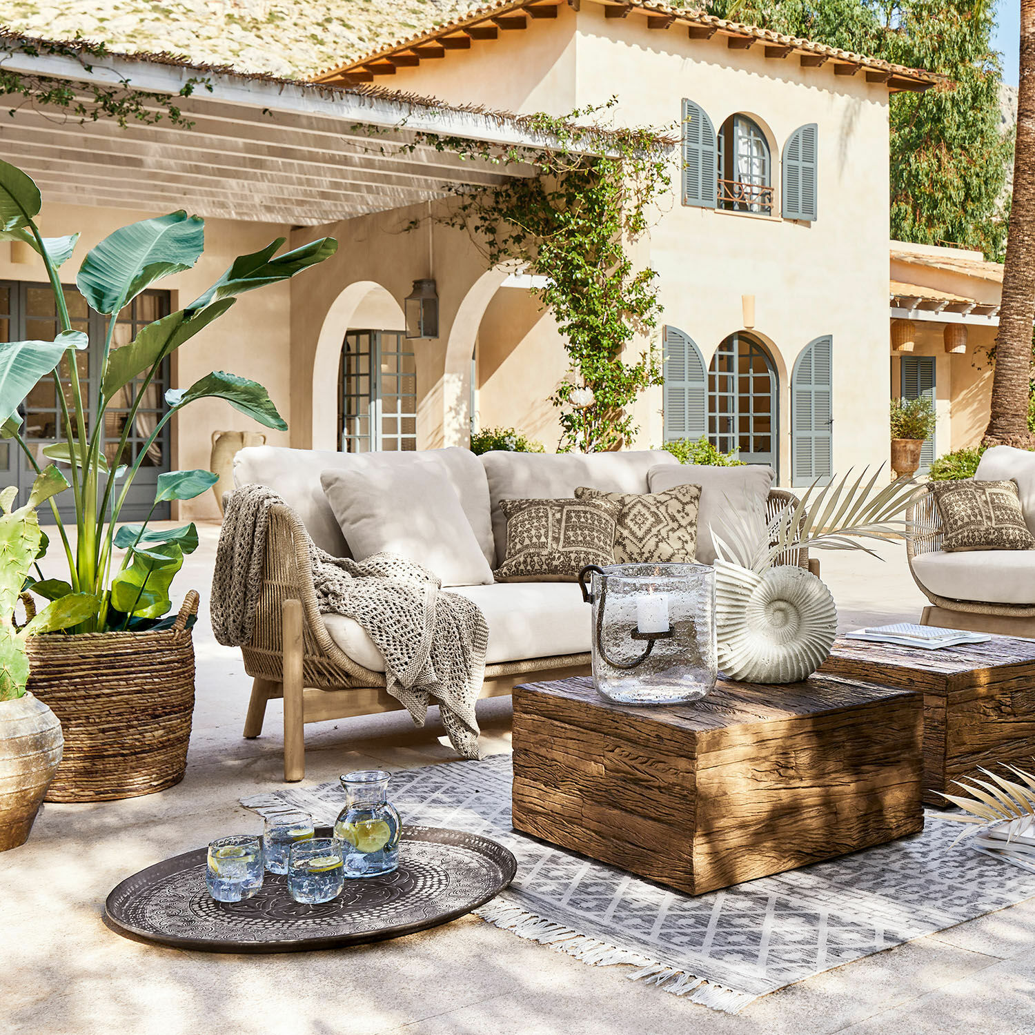 Sofá FSC®-100% Belvidere Conjunto de muebles de exterior con sofá beige, mesa de madera y decoraciones en terraza soleada