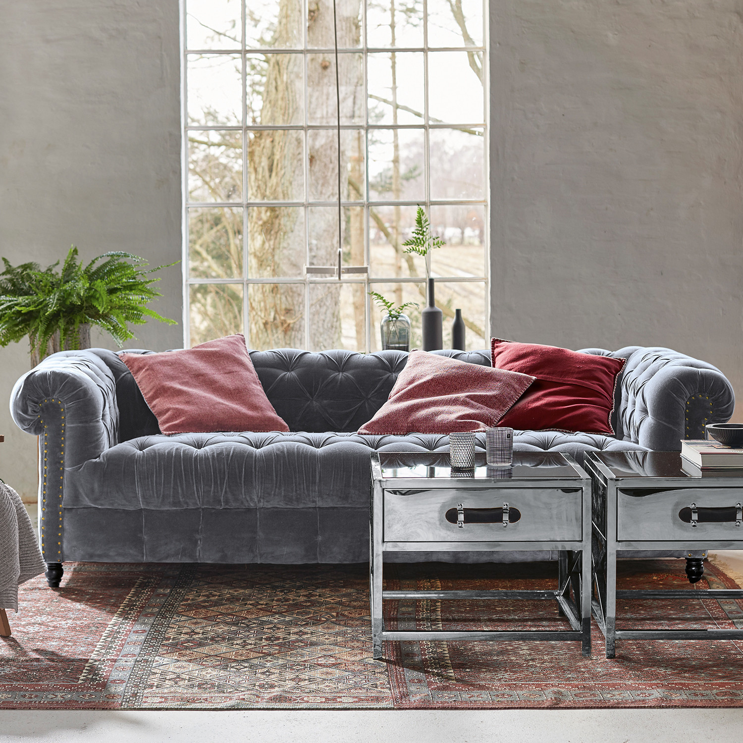 Sofá Parpeville Sofá Chesterfield de terciopelo gris con cojines rojos y mesas auxiliares metálicas sobre alfombra decorativa