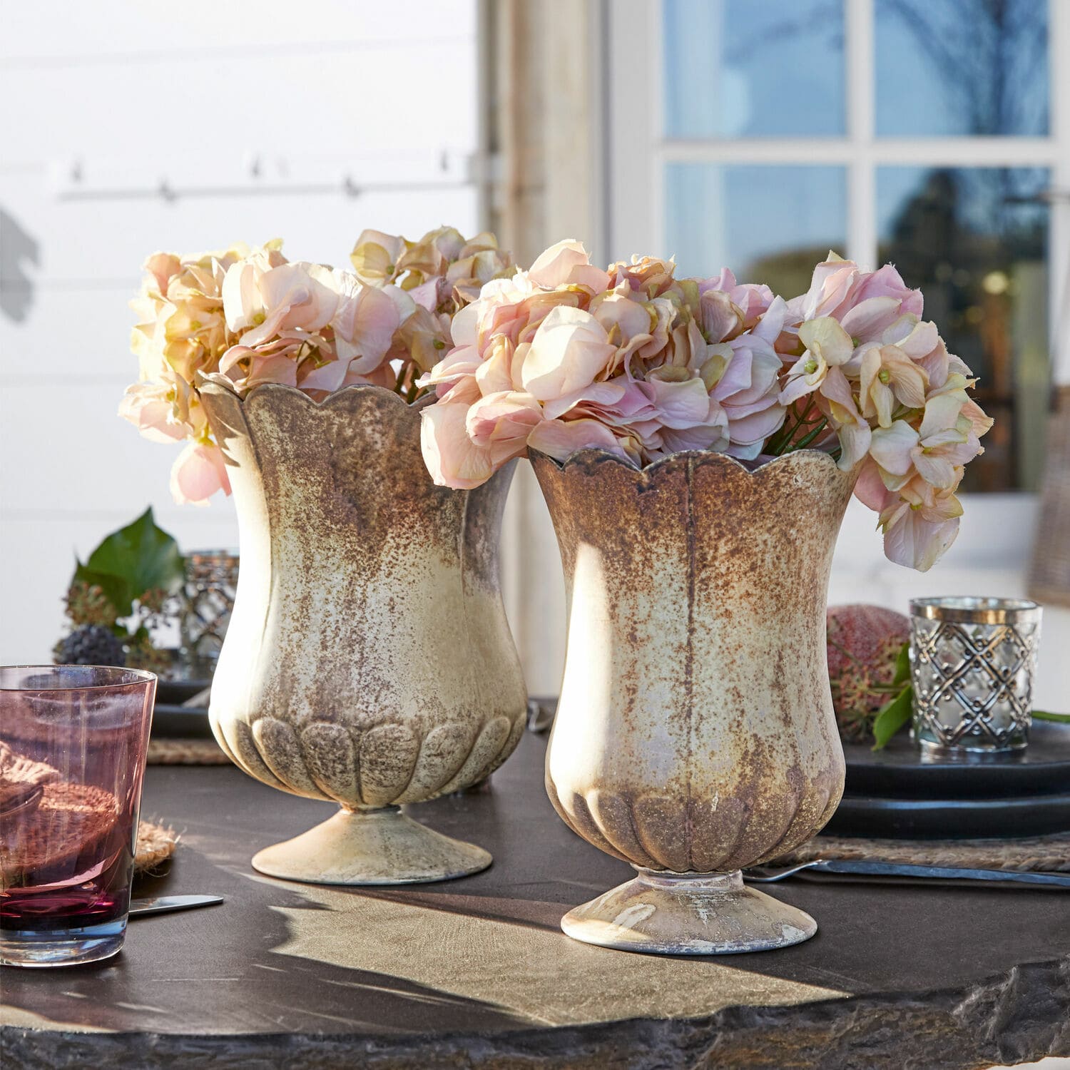 Set de 2 jarrones Wilgard Dos jarrones de cerámica beige y marrón con flores rosas sobre una mesa de jardín