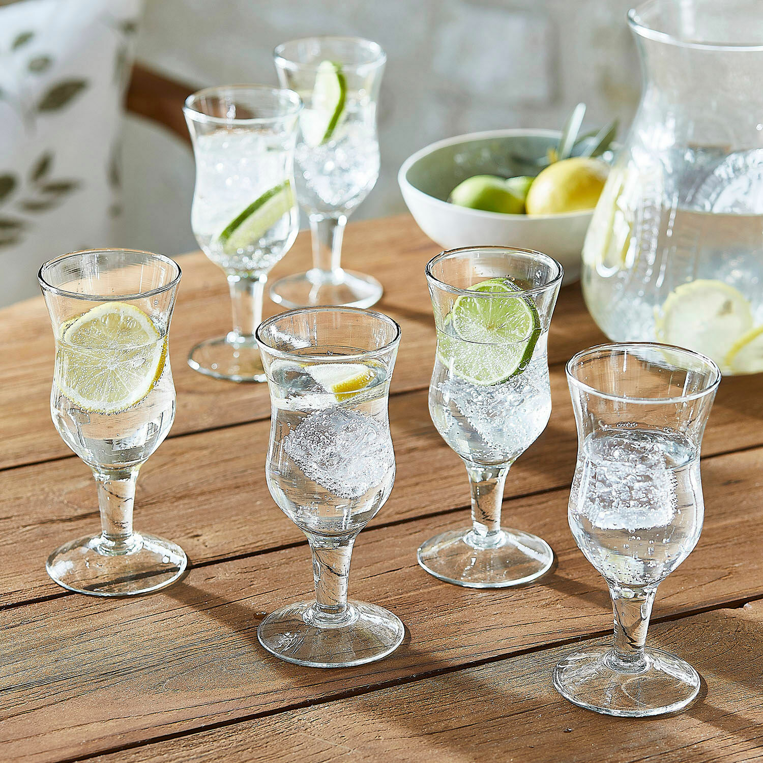 Set de 6 vasos Gaëtane Conjunto de seis vasos transparentes con agua, hielo y rodajas de limón sobre mesa de madera