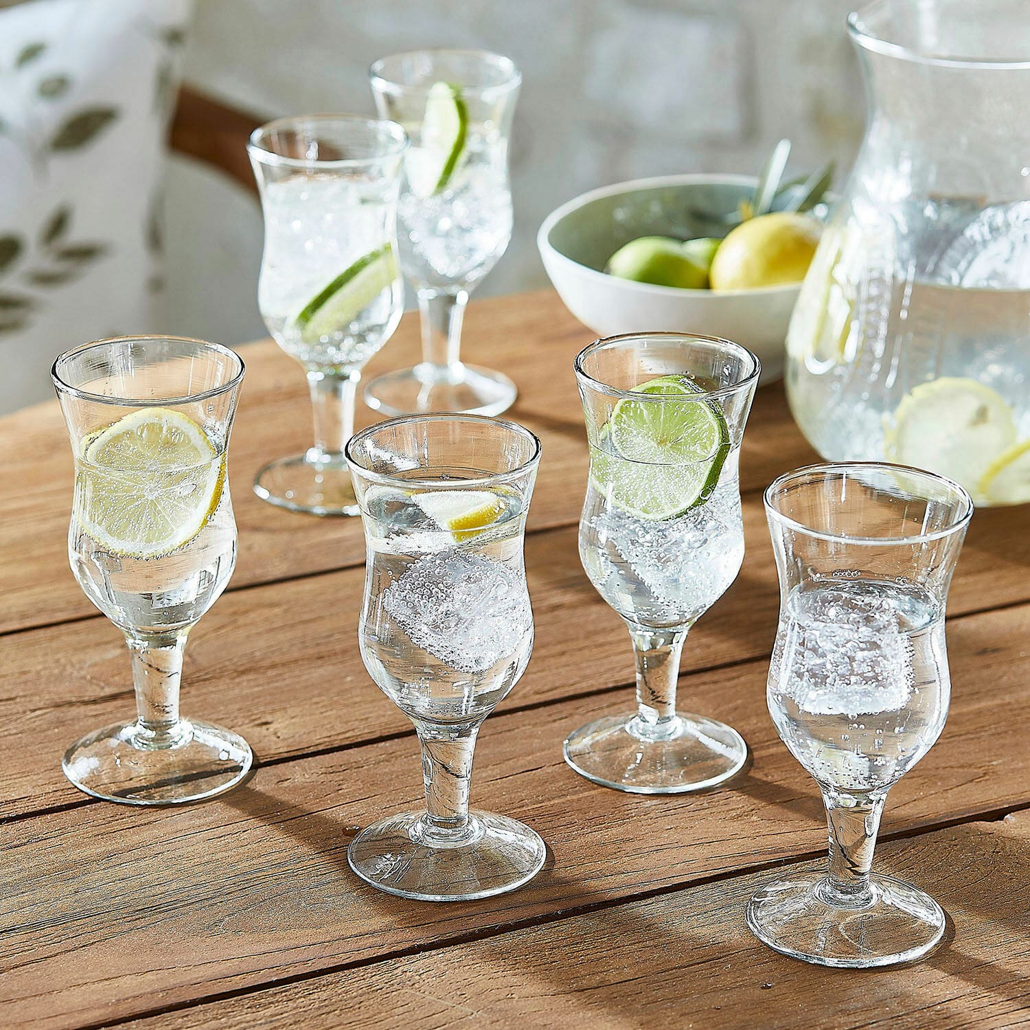 Set de 6 vasos Gaëtane Conjunto de seis vasos transparentes con agua, hielo y rodajas de limón sobre mesa de madera