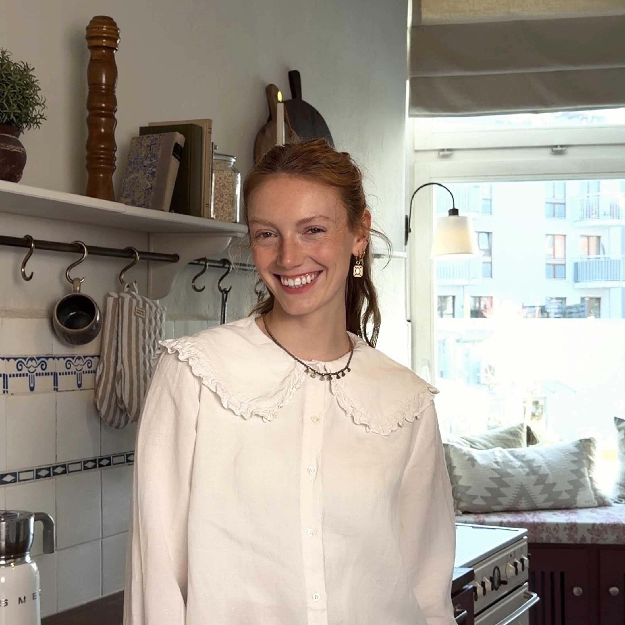 Mujer con blusa blanca con volantes en cocina luminosa con accesorios decorativos y ventana