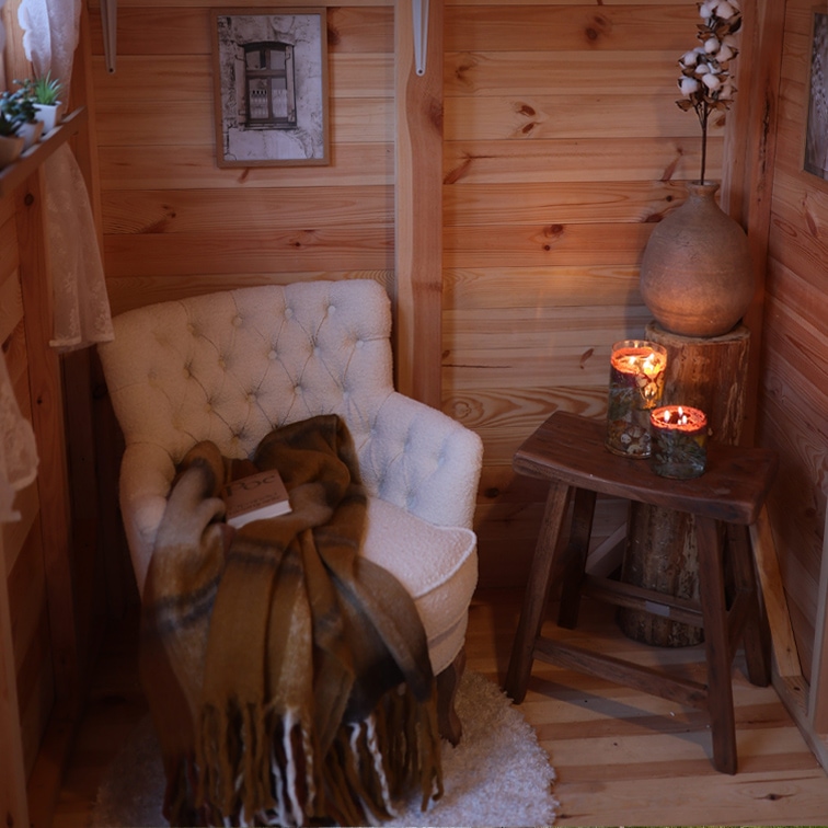 Rincón acogedor con sillón blanco acolchado, manta marrón y taburete de madera con velas encendidas
