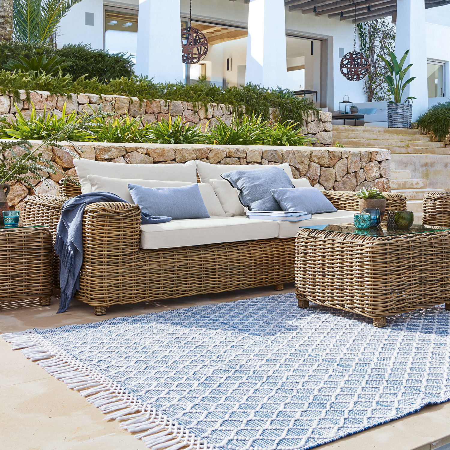 Conjunto de muebles de jardín de ratán natural con cojines crema y alfombra azul con patrón