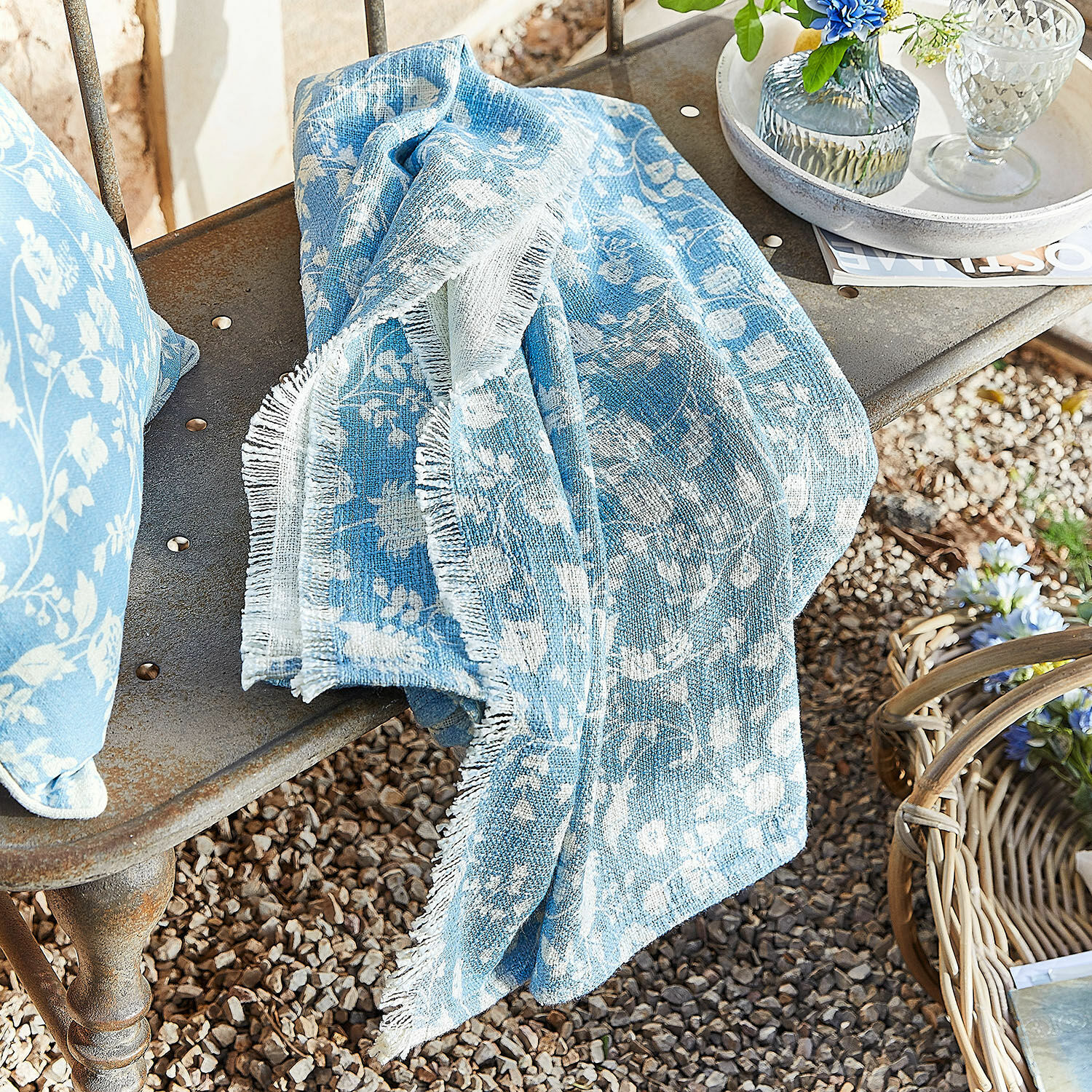 Plaid Corvelique Manta de algodón azul con diseño floral blanco sobre banco metálico en jardín