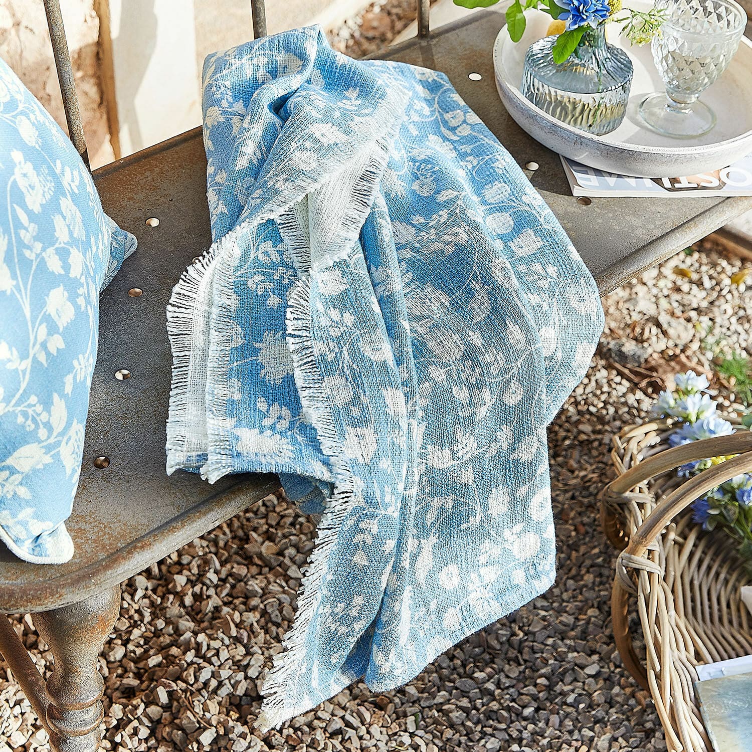 Plaid Corvelique Manta de algodón azul con diseño floral blanco sobre banco metálico en jardín