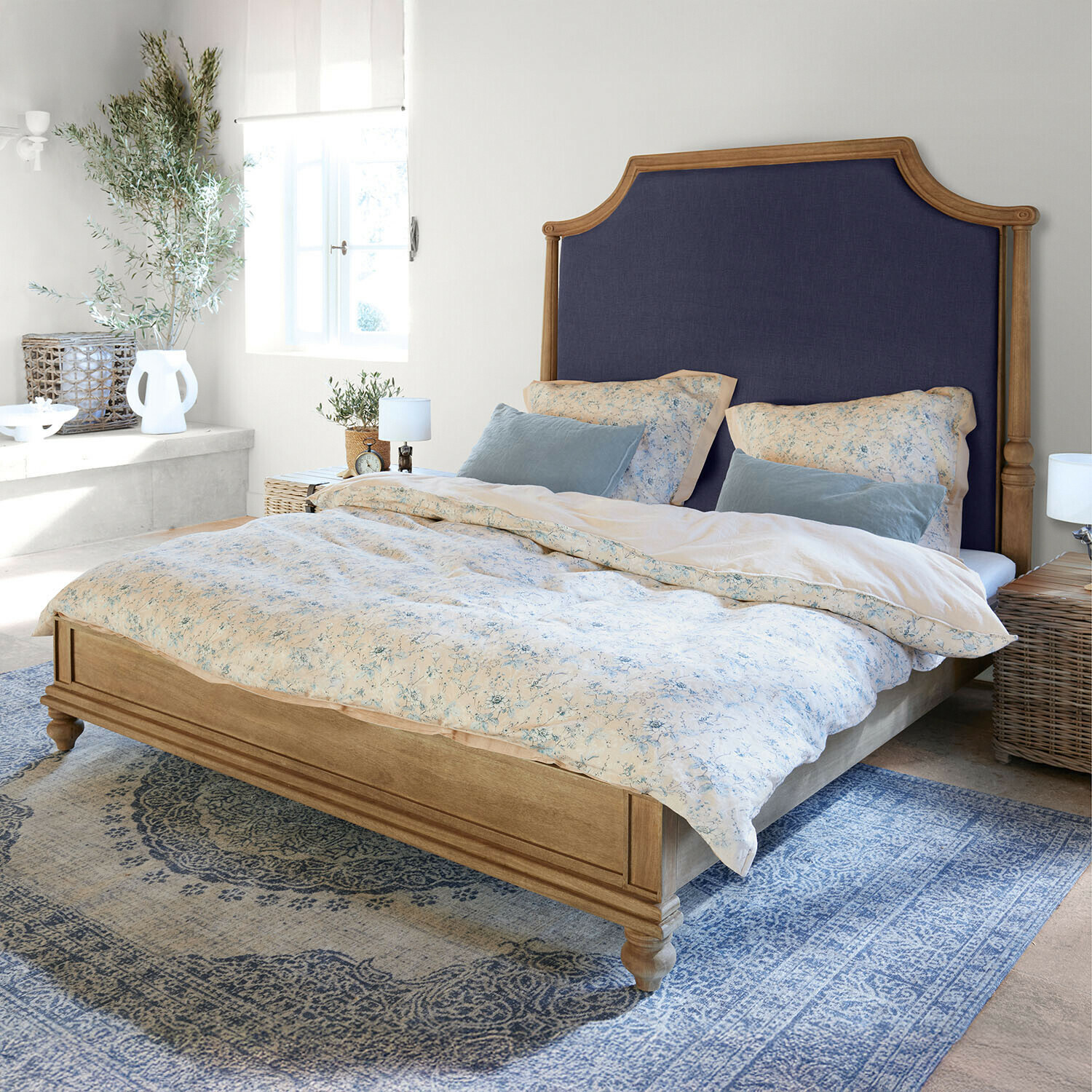 Cama de madera con cabecero tapizado azul marino en dormitorio luminoso con alfombra azul