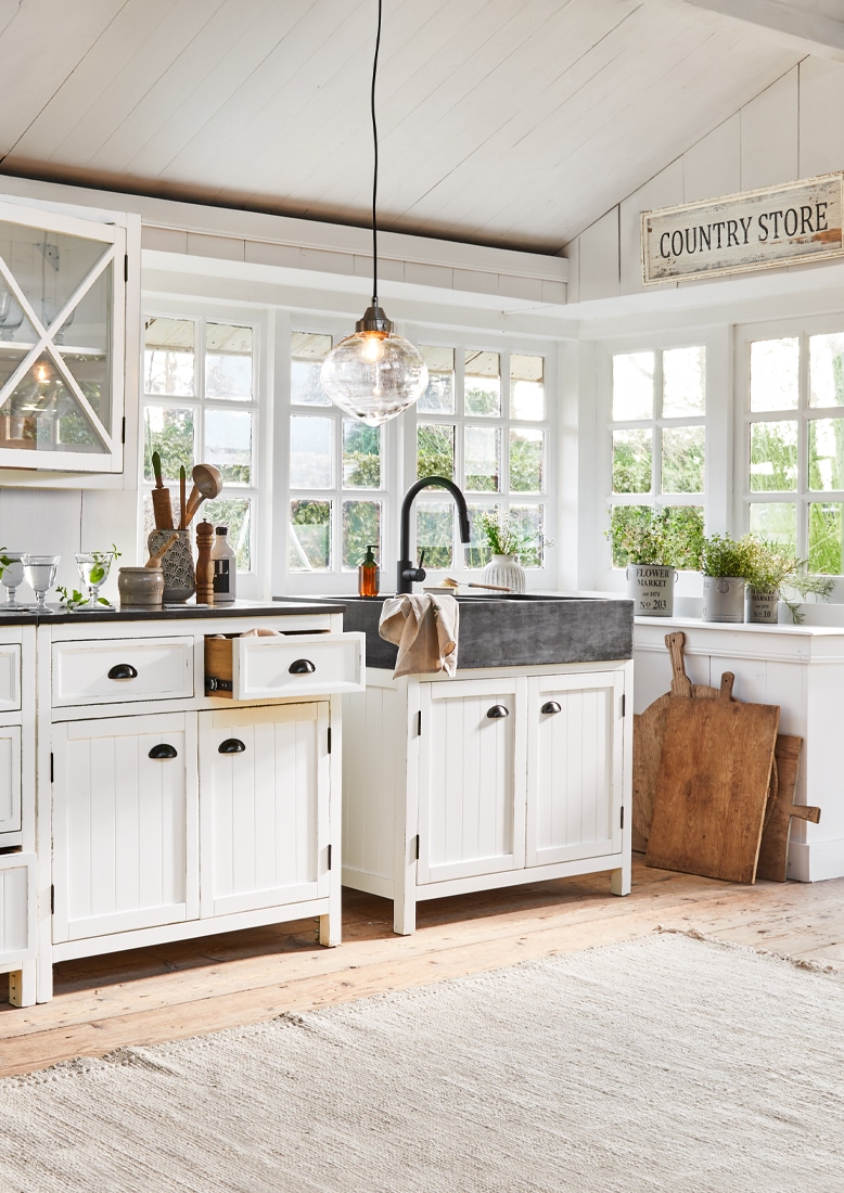 Cocina rústica con armarios blancos de madera y fregadero negro de piedra, decoración con plantas