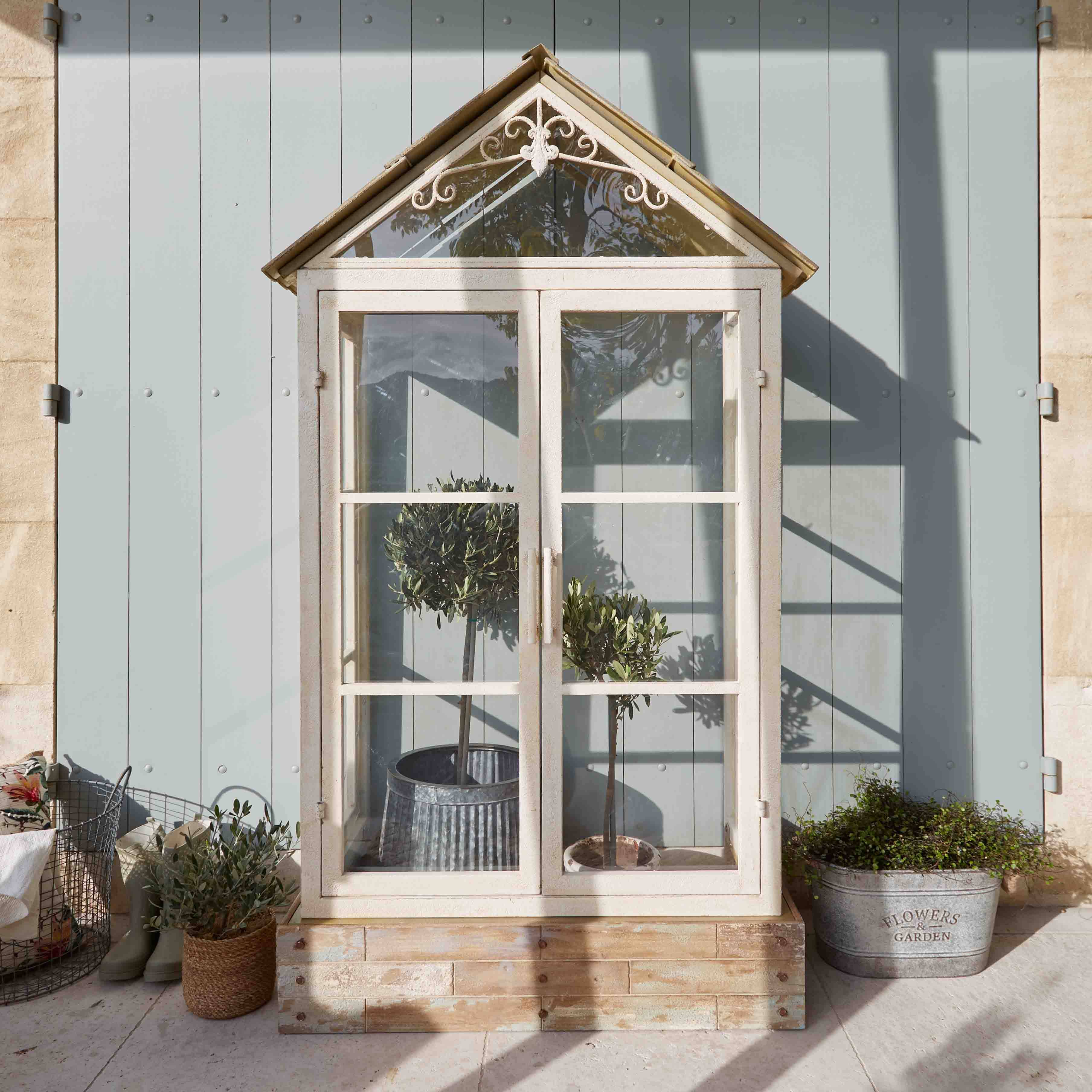 Invernadero blanco de madera con techo decorativo y plantas en macetas en terraza soleada