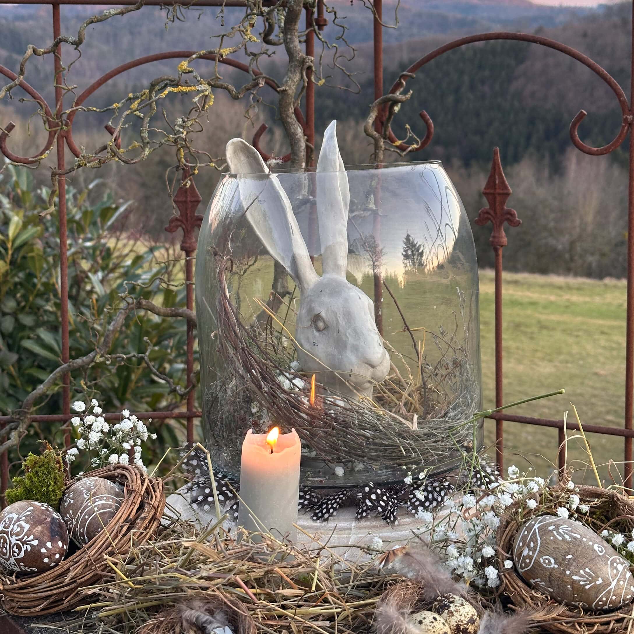 Decoración de Pascua con conejo de cerámica blanca en recipiente de vidrio y vela encendida rústica