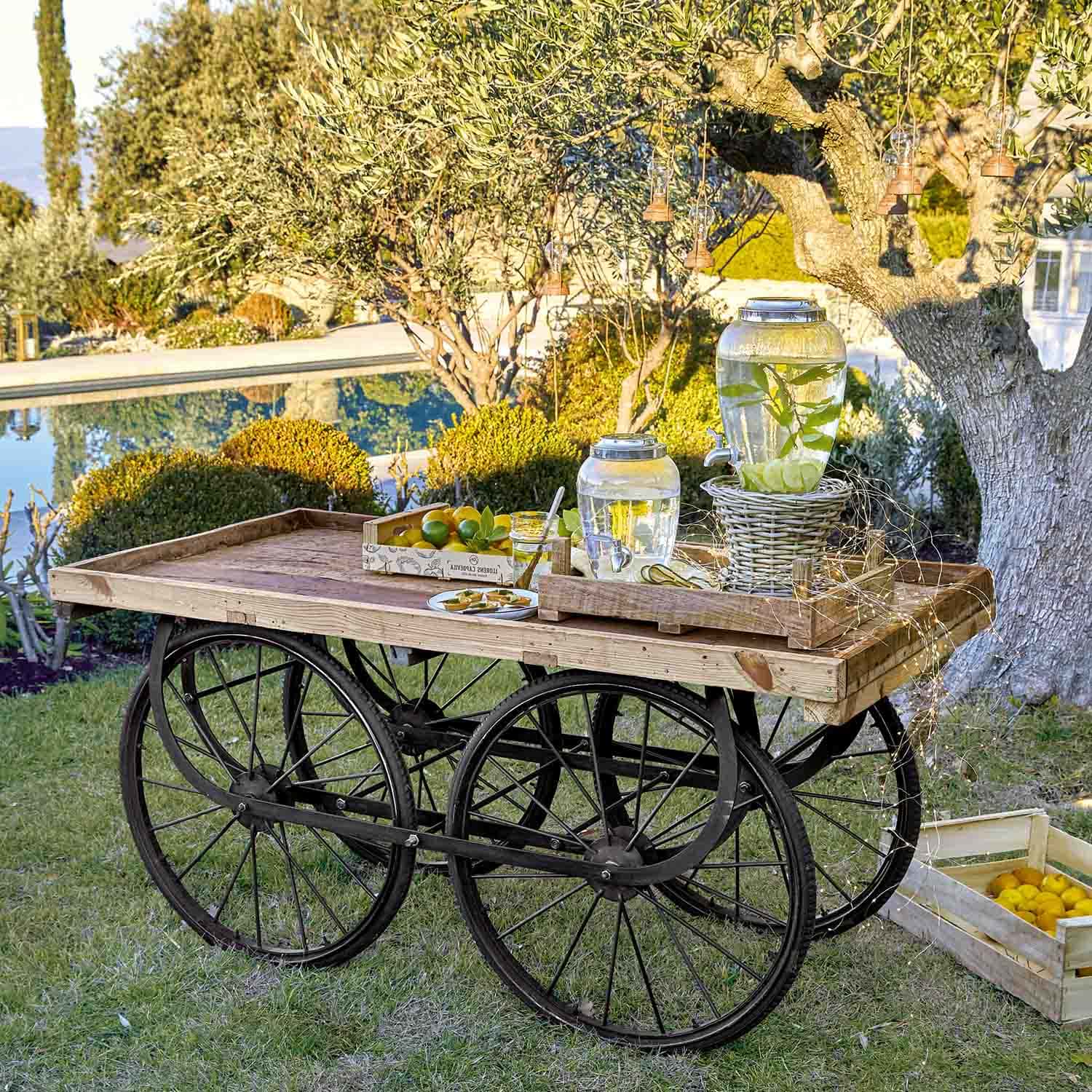 Carro de madera con ruedas negras con dispensadores de agua con limón en un jardín