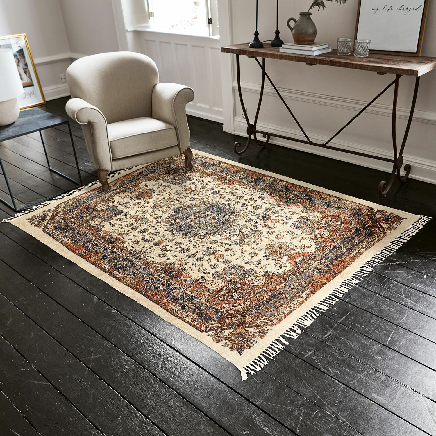 Alfombra Aleixo Alfombra decorativa con flecos en tonos crema y marrón sobre suelo de madera oscura