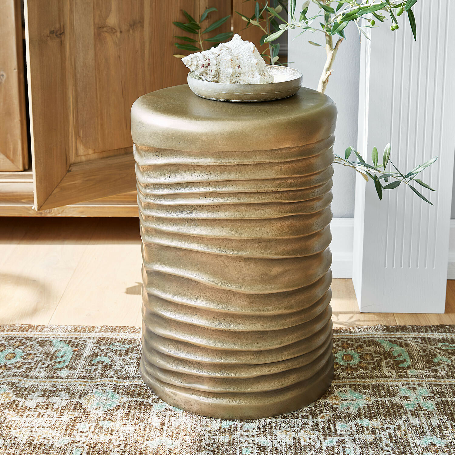 Mesa auxiliar de metal dorado con textura ondulada sobre alfombra en interior luminoso