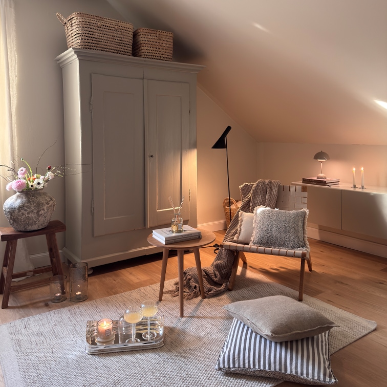 Sala acogedora con sillón beige, mesa de madera y armario bajo techo inclinado, decoraciones y lámparas