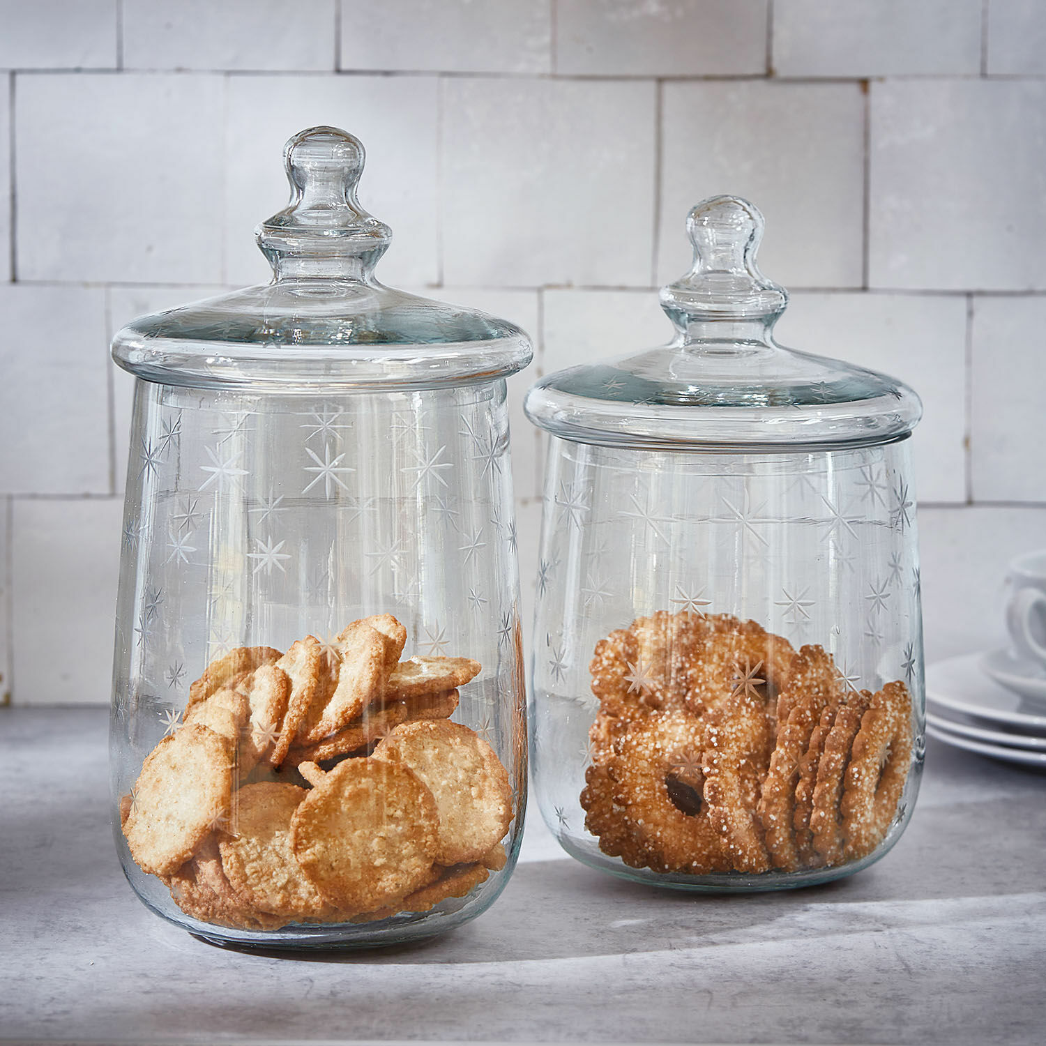 Set de 2 tarros de cristal Valerico Dos tarros de vidrio transparente con tapas, decorados con estrellas, llenos de galletas