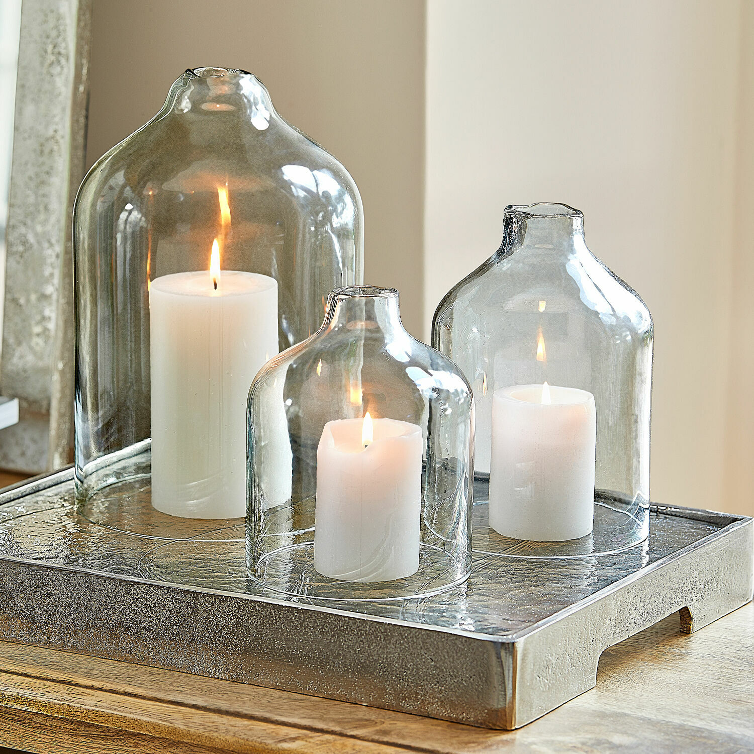 Set de 4 velas Braga Tres velas blancas bajo campanas de vidrio transparente sobre bandeja decorativa de metal