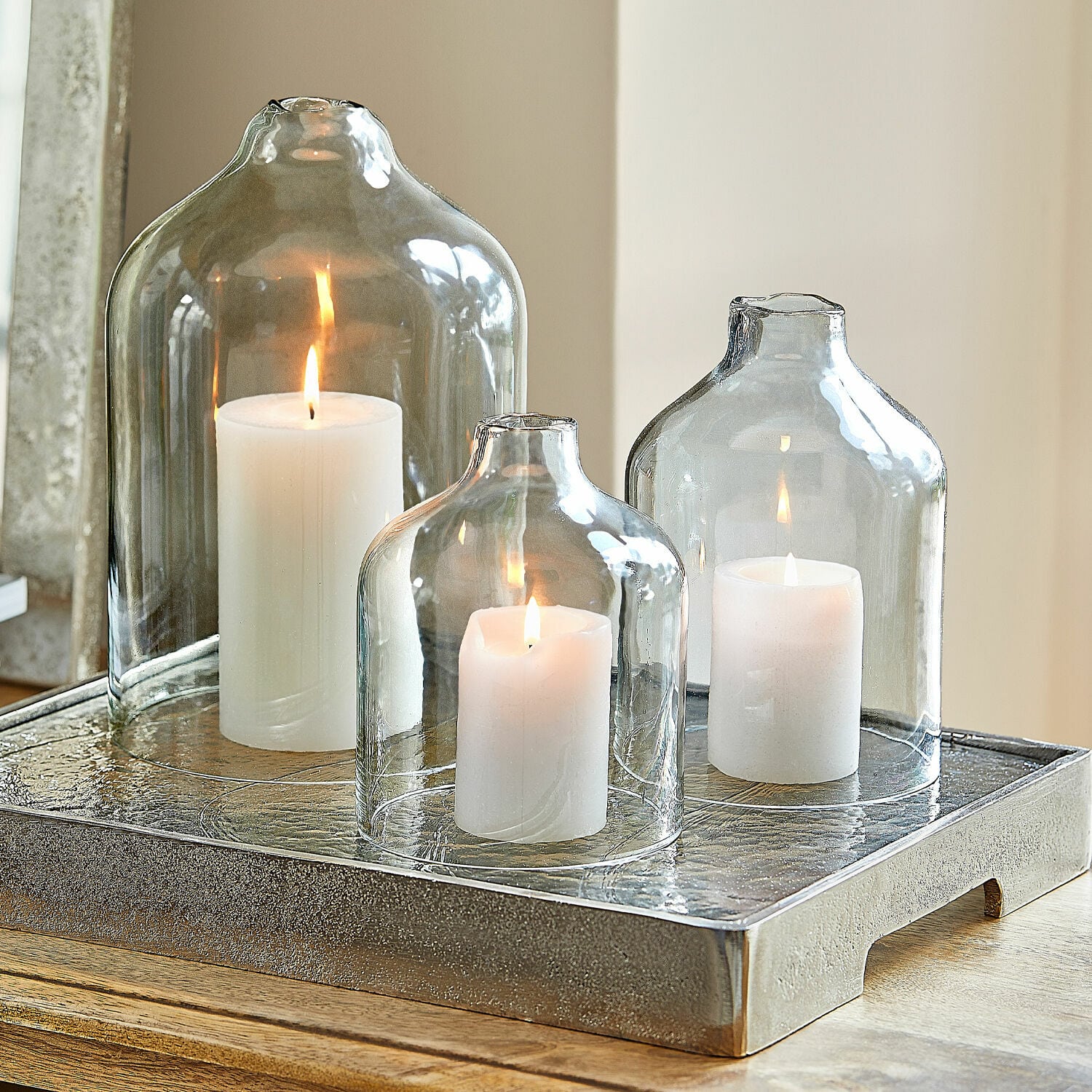 Set de 4 velas Braga Tres velas blancas bajo campanas de vidrio transparente sobre bandeja decorativa de metal
