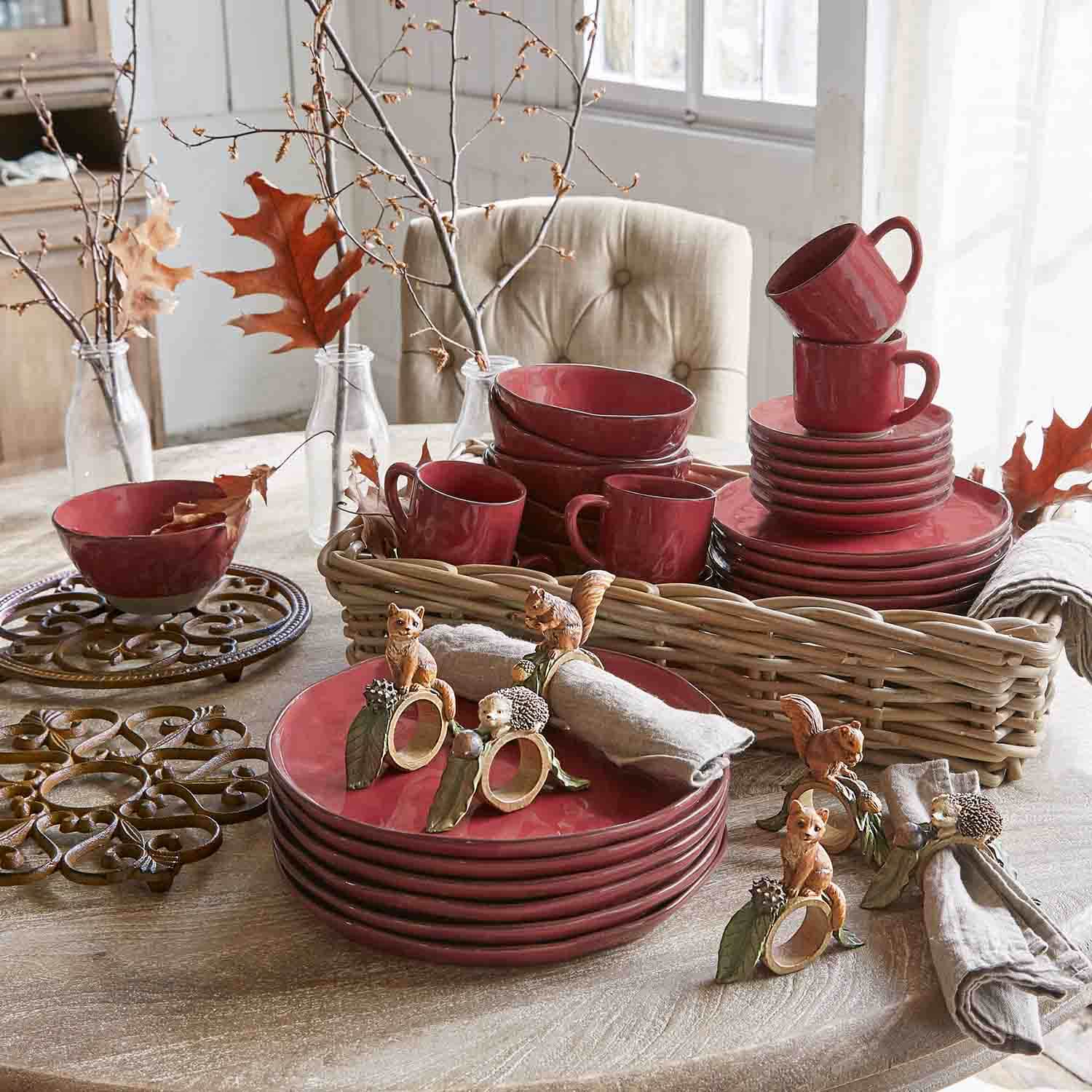 Juego de vajilla de cerámica roja con tazas y platos sobre mesa de madera con decoración otoñal