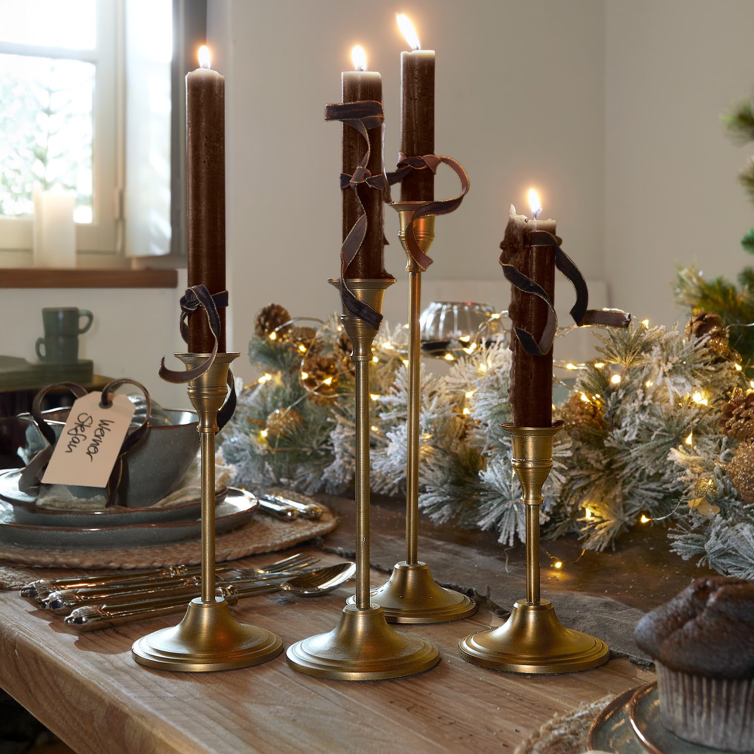 Conjunto de cuatro candelabros dorados con velas marrones y cintas decorativas sobre mesa de madera