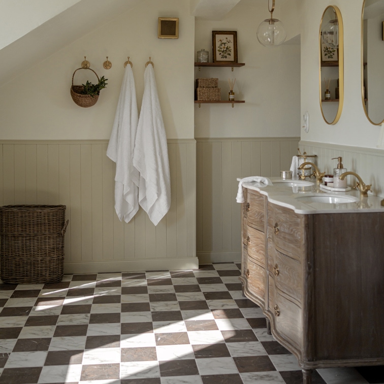 Baño con suelo de mármol a cuadros, mueble de madera y toallas blancas colgadas en ganchos