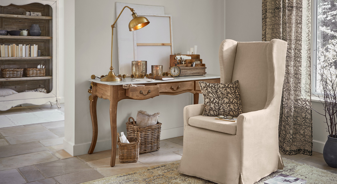 Sillón orejero beige con cojín y escritorio de madera con lámpara en sala acogedora con decoración natural