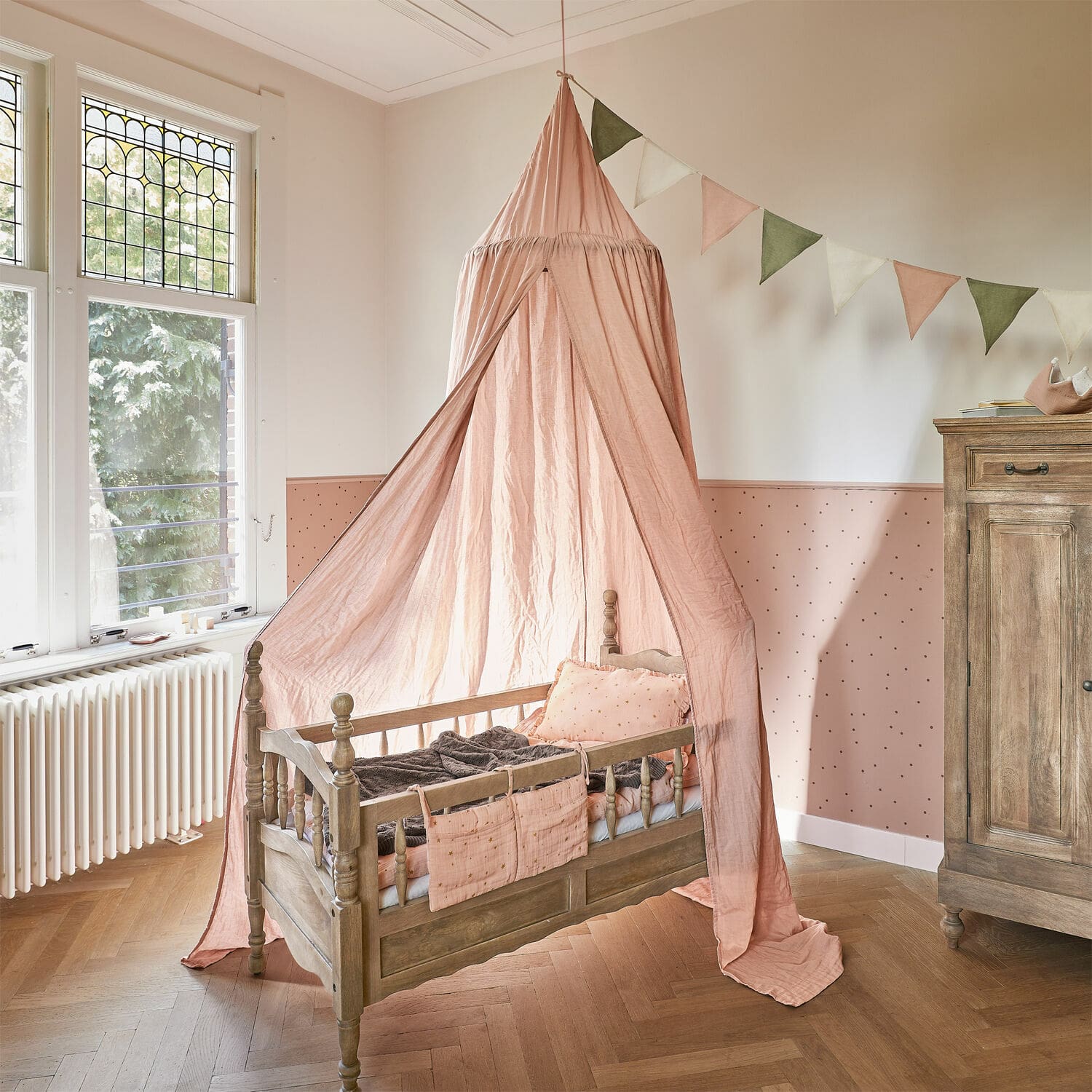 Dosel Lisonne Cuna infantil de madera con dosel rosa y cojines decorativos en habitación infantil luminosa