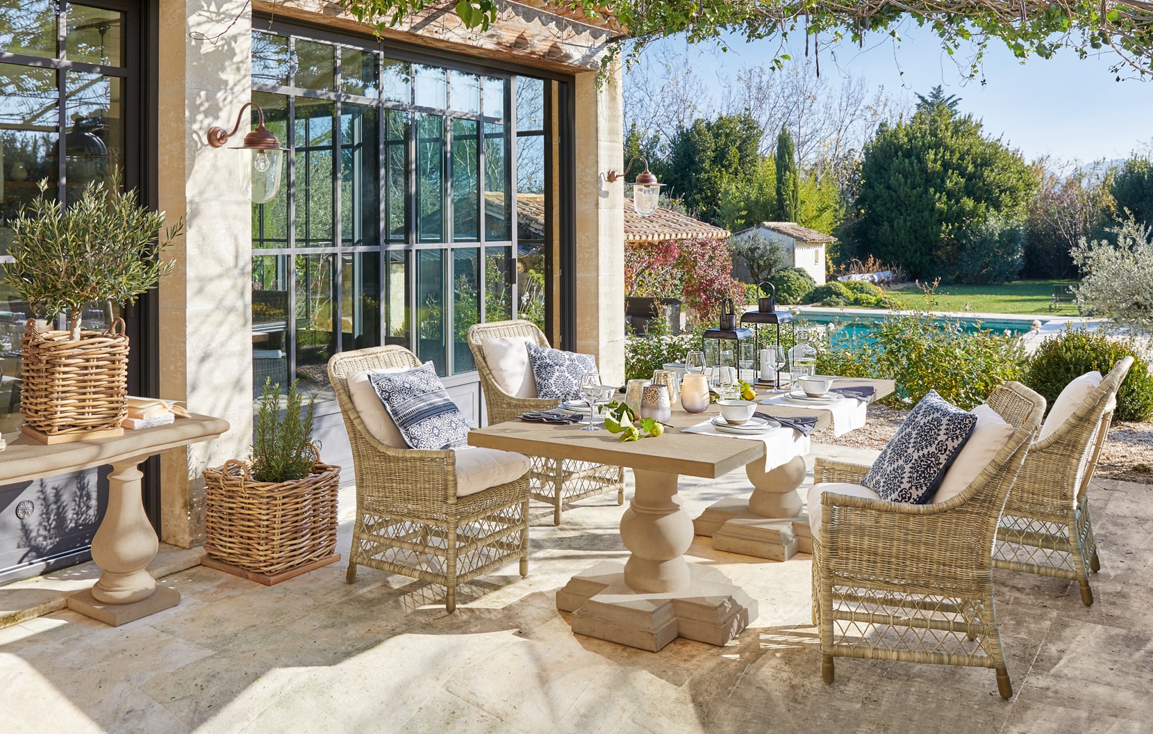 Acogedora terraza con muebles de ratán y mesa de piedra en estilo mediterráneo con vista a la piscina
