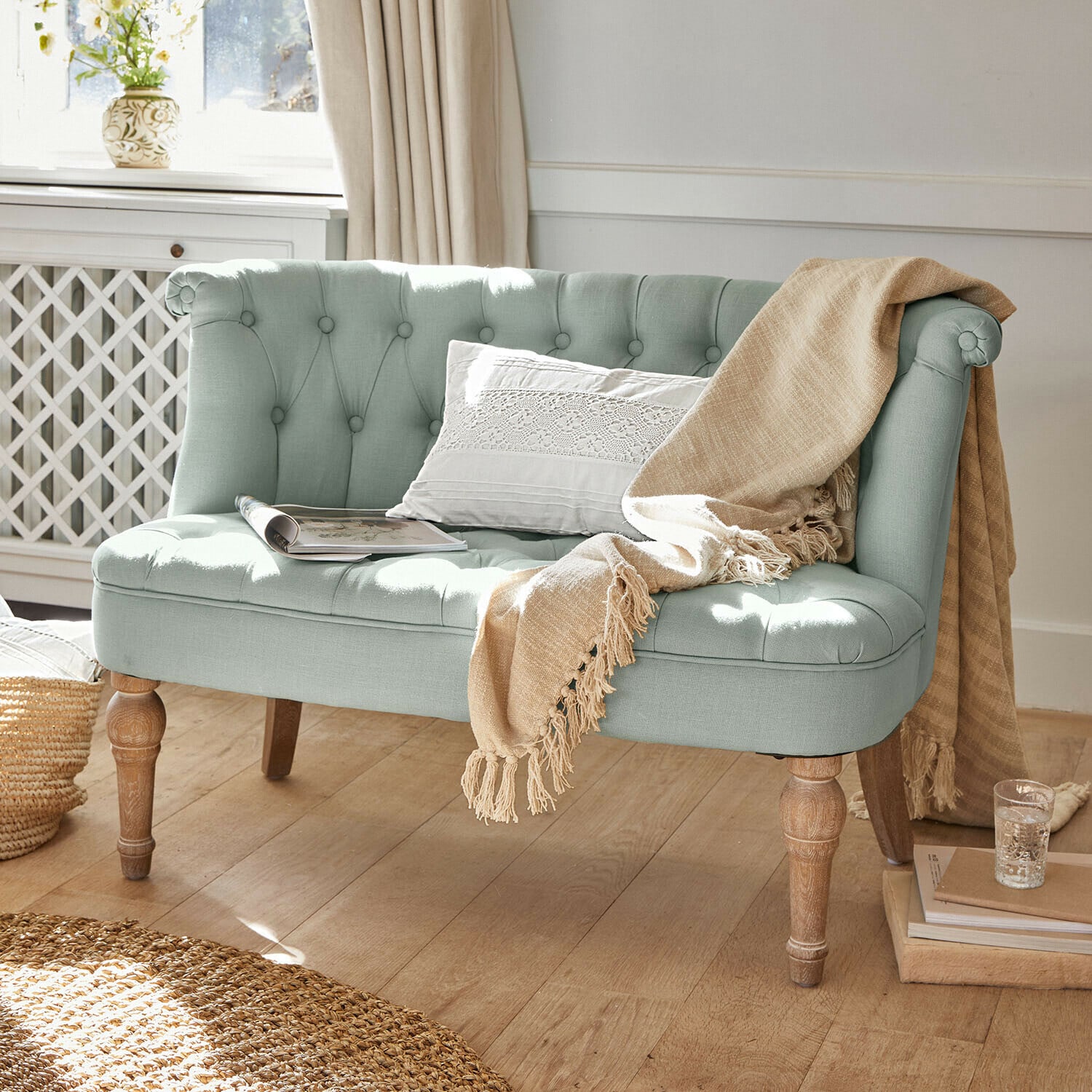 Sofá Weralin Sofá tapizado verde menta con patas de madera, manta beige y cojín blanco, estilo vintage