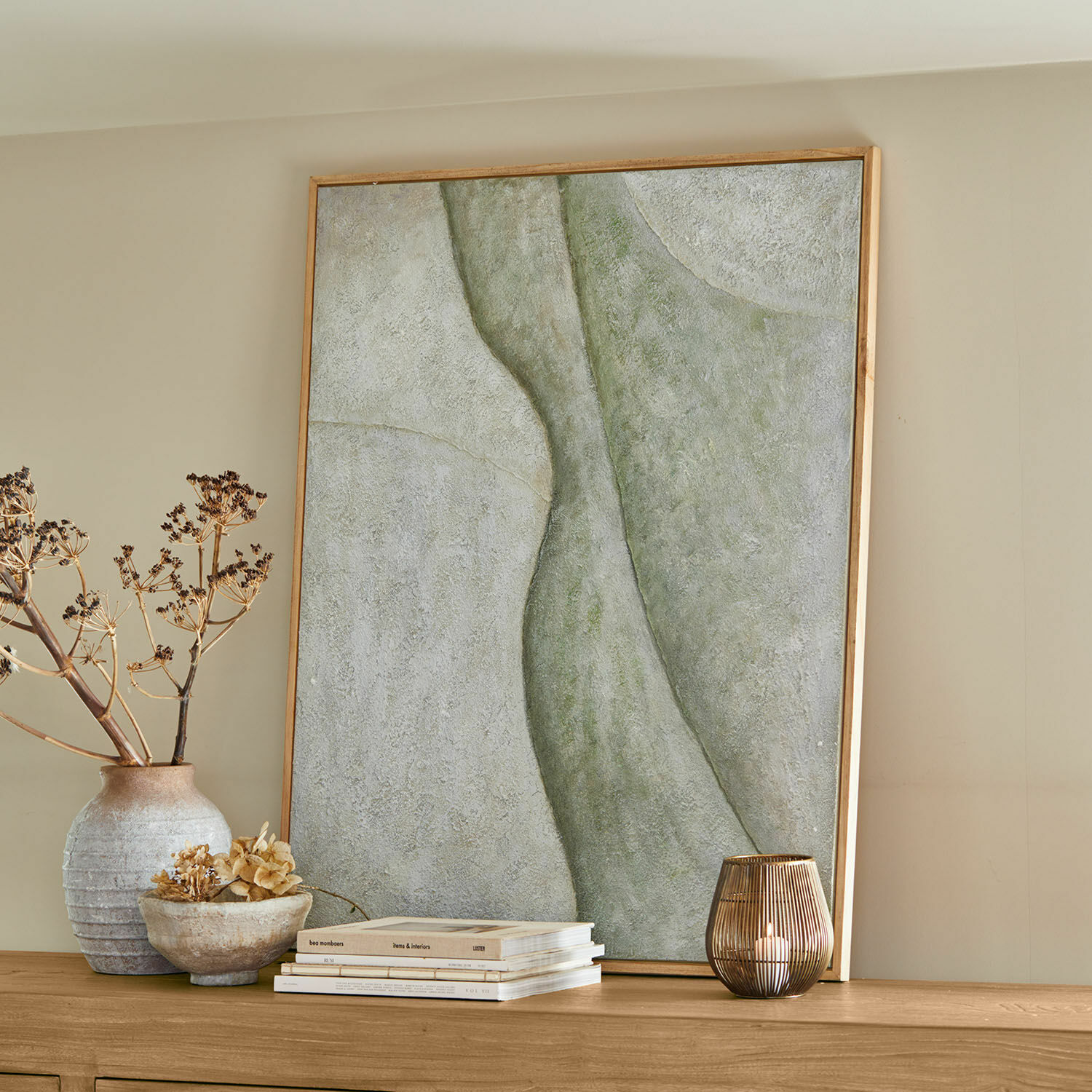 Cuadro decorativo con diseño abstracto en tonos verdes y grises sobre mueble de madera clara
