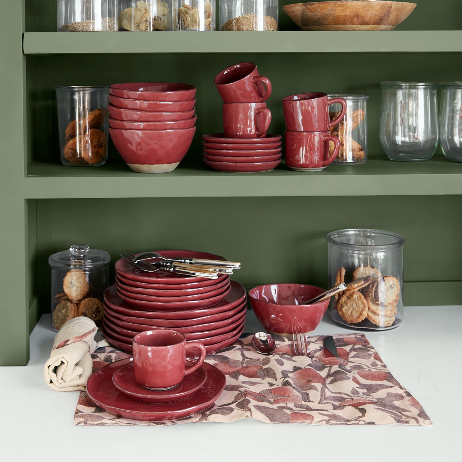 Juego de vajilla de cerámica roja en estantería verde con galletas en recipientes de vidrio