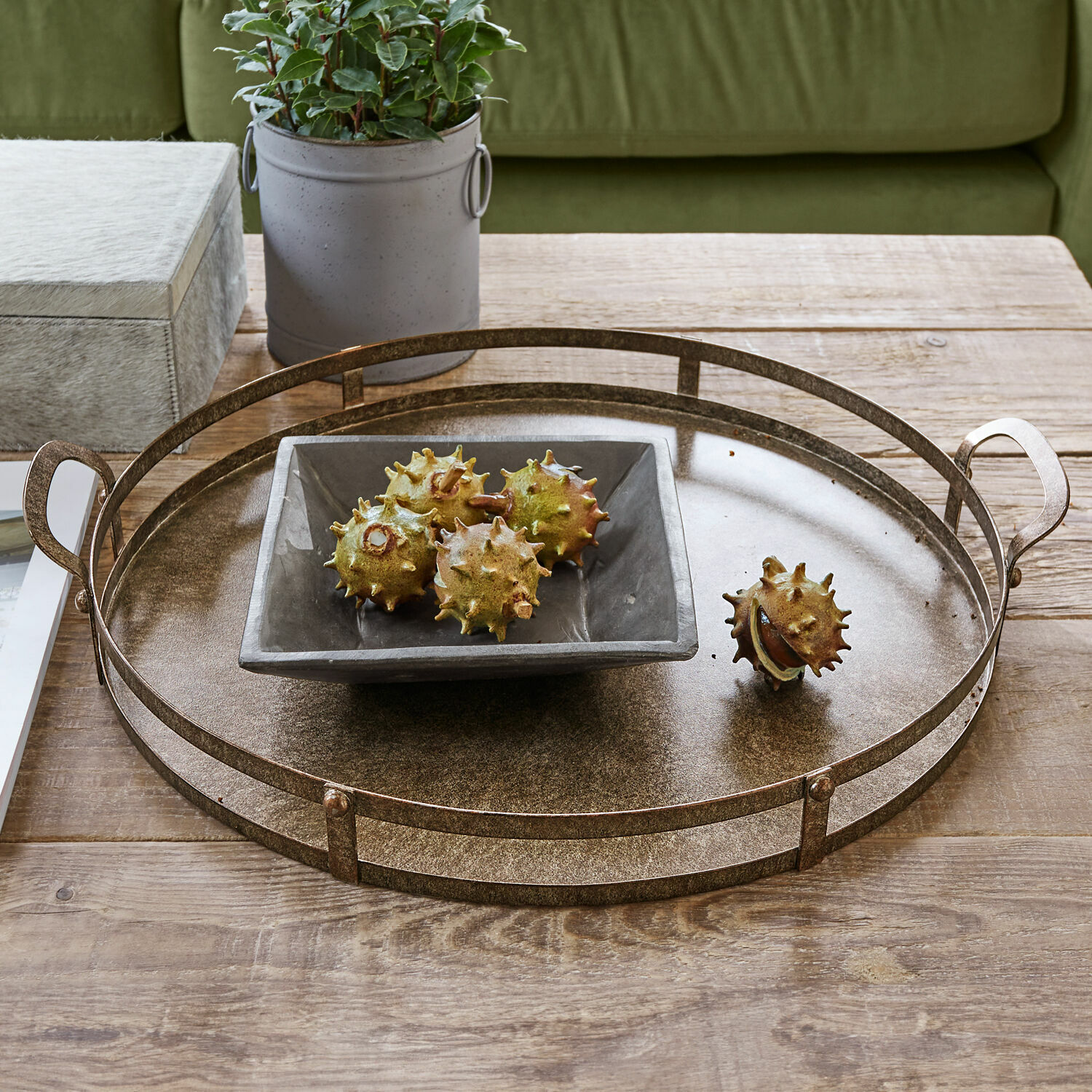 Bandeja Aquivar Bandeja redonda de metal color latón sobre mesa de madera con cuenco de cerámica y castañas decorativas