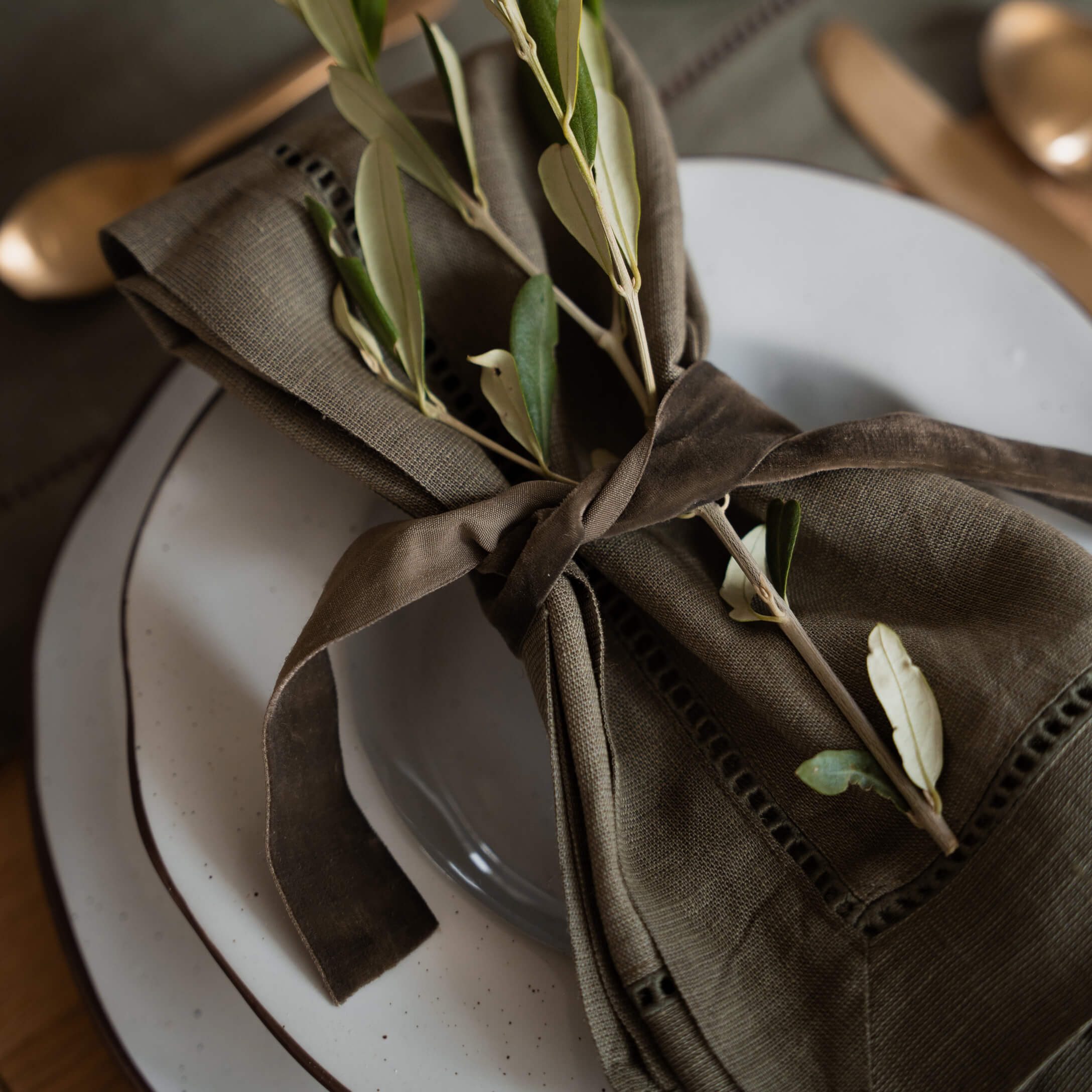 Servilleta de lino marrón con ramas verdes sobre plato blanco para decoración de mesa