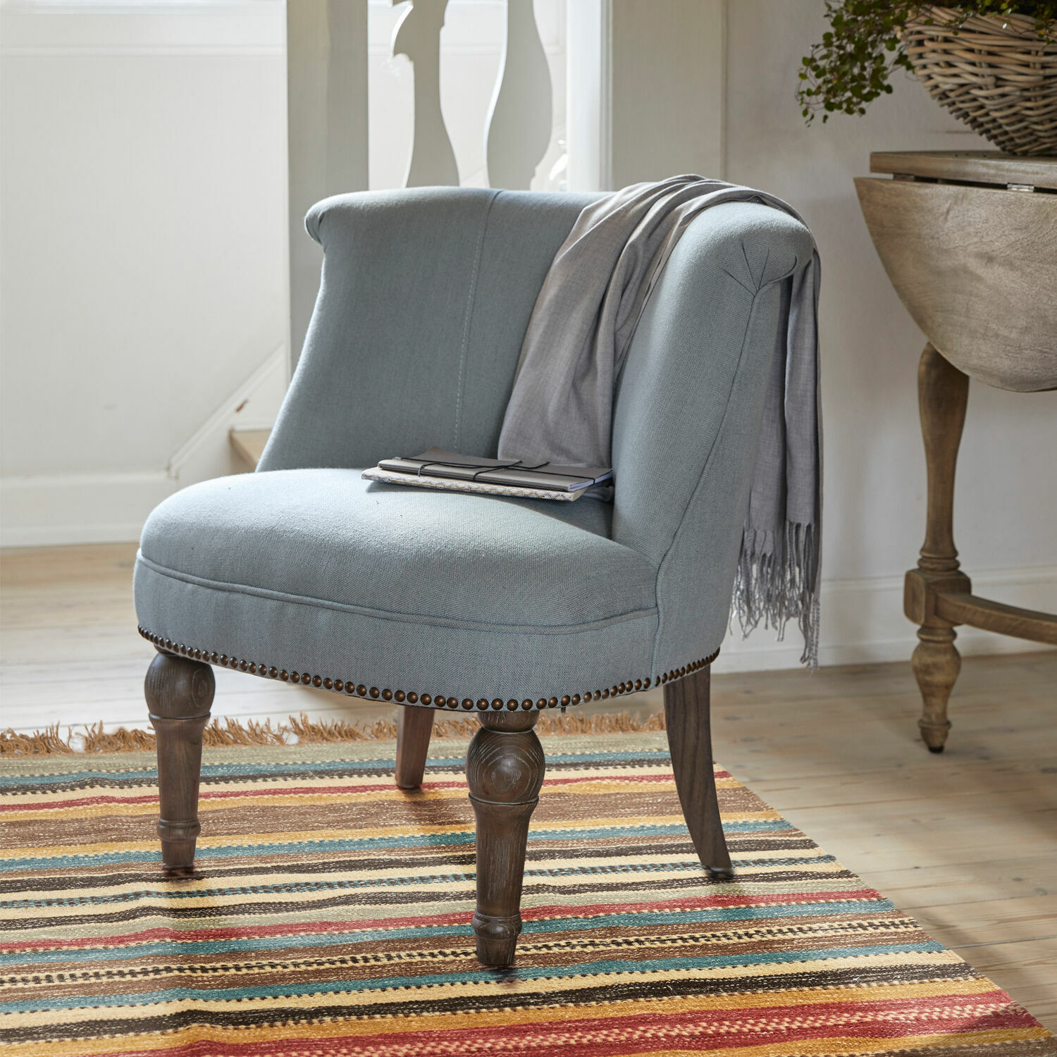 Sillón Francet Sillón tapizado gris con patas de madera sobre alfombra colorida en interior luminoso