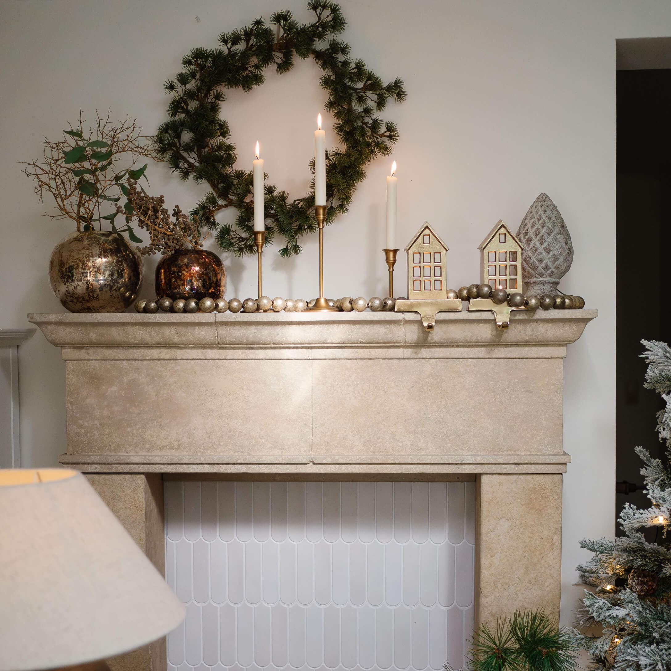 Chimenea de piedra beige con corona verde, candelabros dorados y decoraciones navideñas elegantes