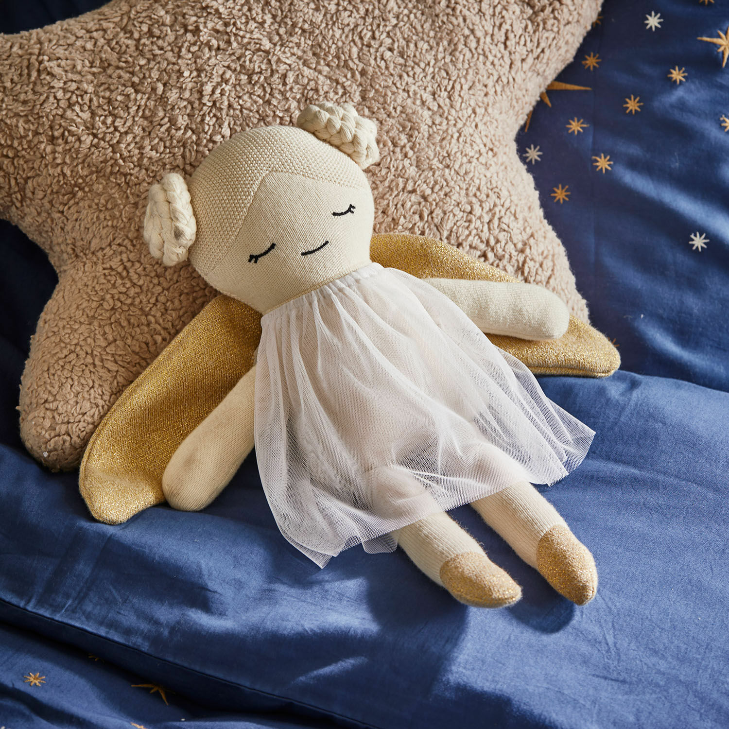 Muñeca de trapo Valonna Muñeca ángel beige de tela con vestido de tul blanco y alas doradas sobre ropa de cama azul con estrellas