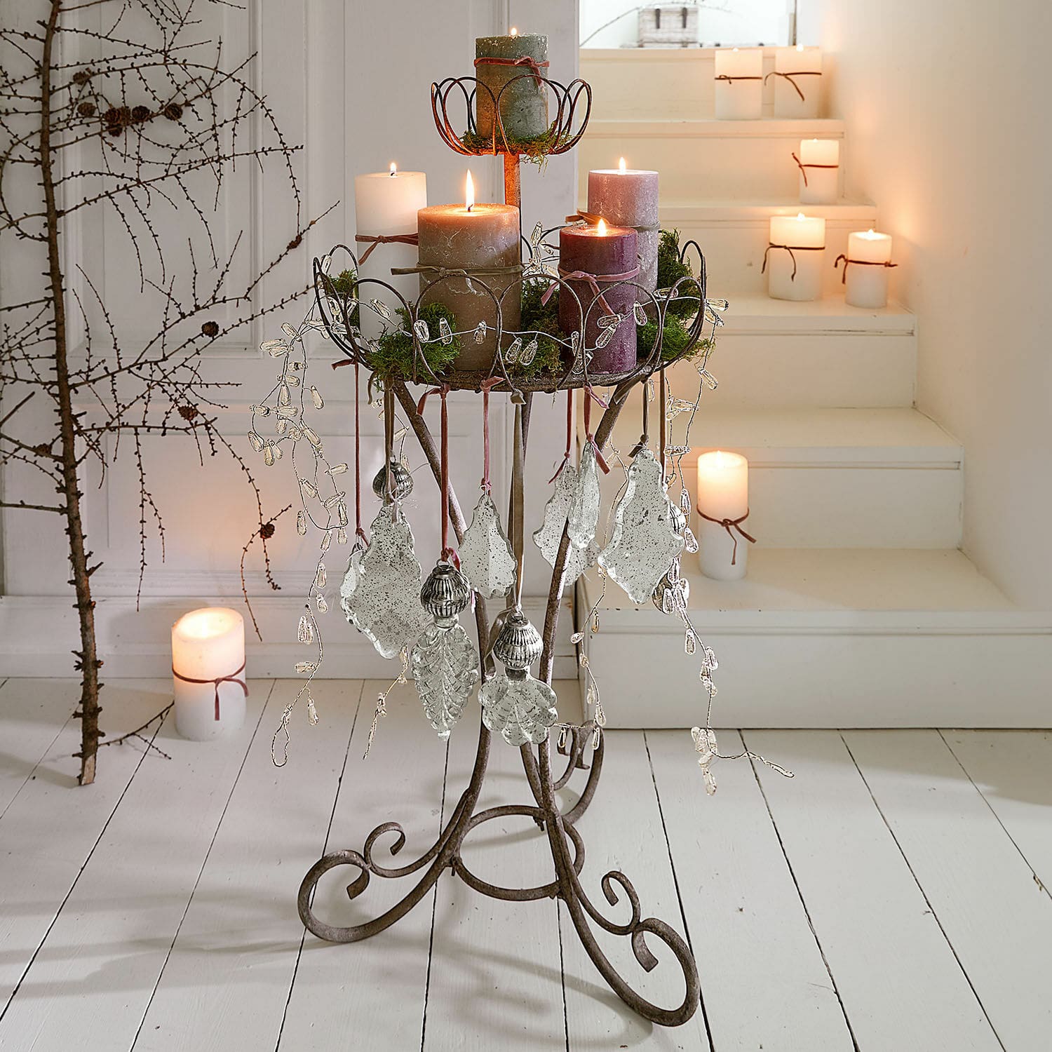 Soporte decorativo Mélissant Soporte metálico con adornos y velas en tonos naturales sobre suelo y escaleras blancas