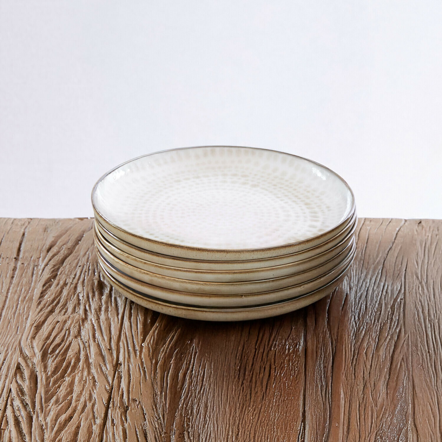 Set de 6 platos de postre Marnis Conjunto de seis platos de cerámica blanca con diseño sutil y borde marrón sobre mesa de madera