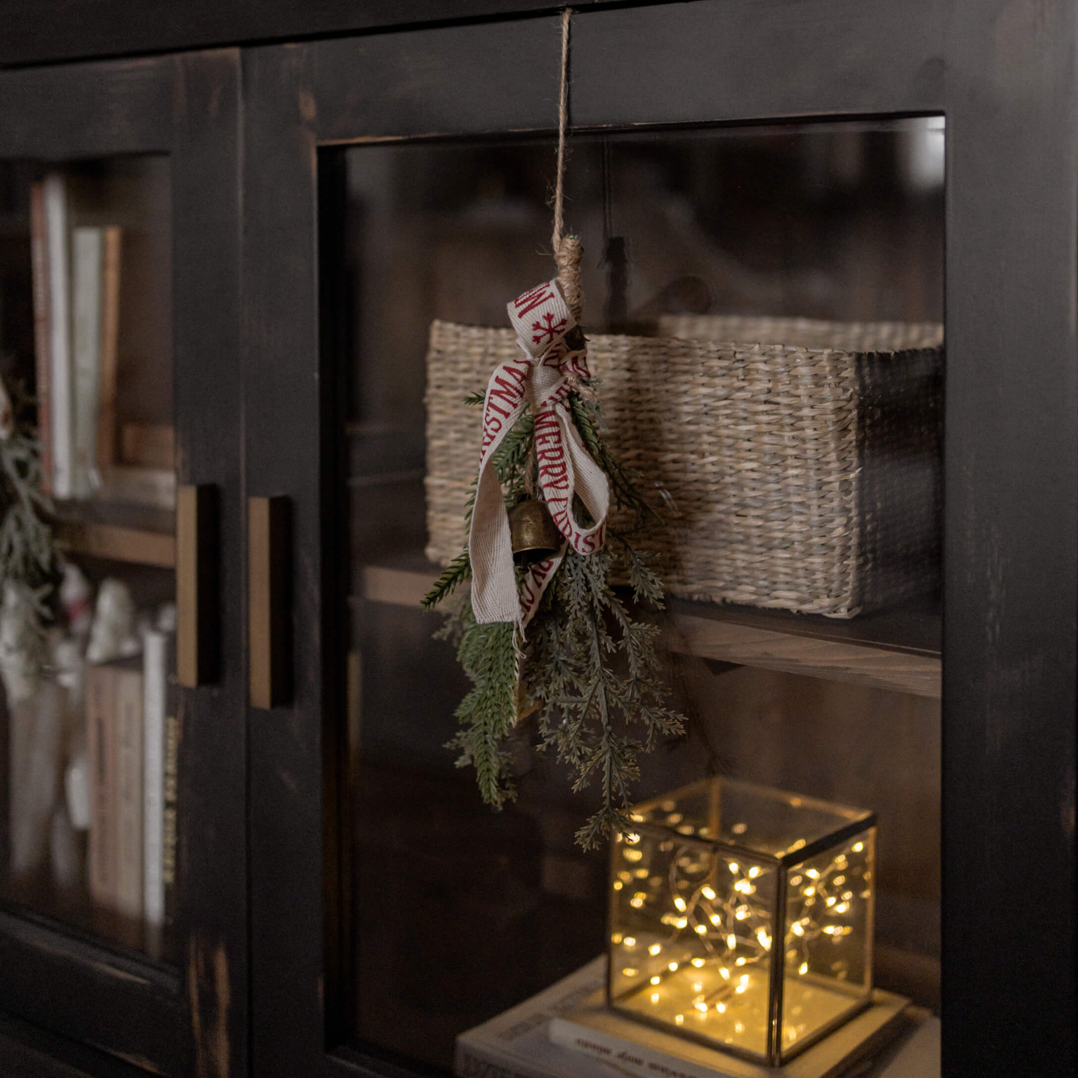 Decoración navideña con ramas verdes, campana y lazo en mueble negro con cesta y luz LED
