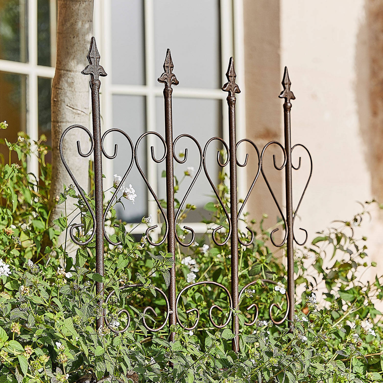 Enrejado Nectarise Valla de jardín de metal marrón óxido con diseño de corazón, rodeada de plantas verdes y flores blancas
