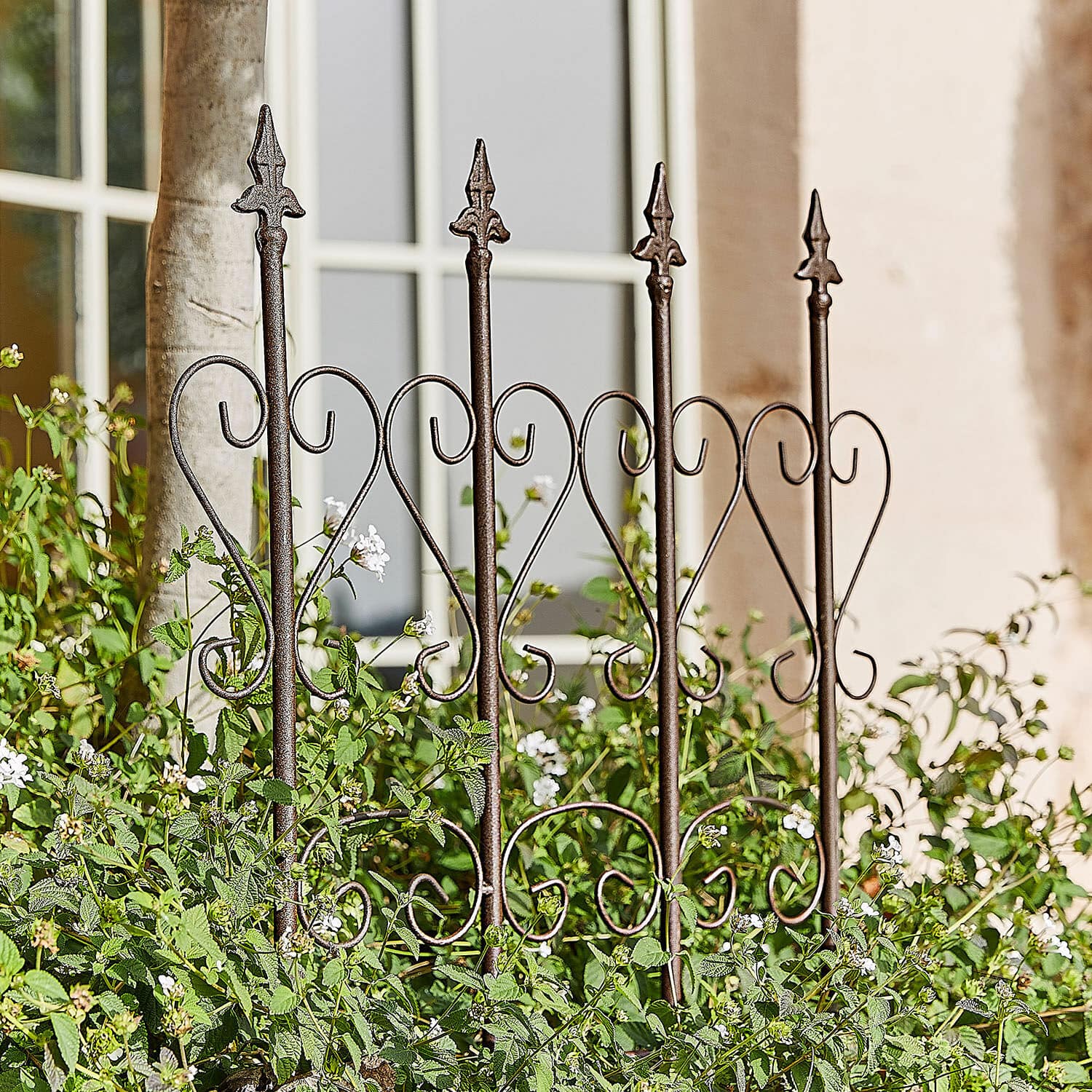 Enrejado Nectarise Valla de jardín de metal marrón óxido con diseño de corazón, rodeada de plantas verdes y flores blancas