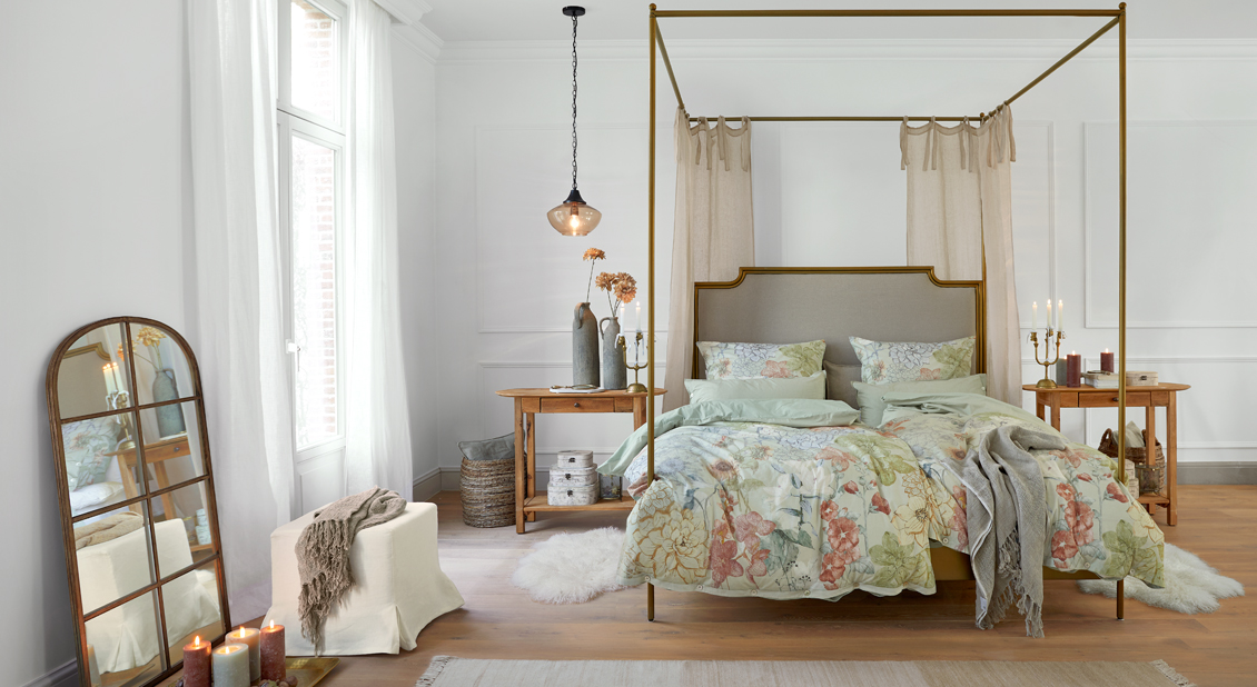 Cama con dosel de metal dorado y ropa de cama floral en dormitorio luminoso y acogedor