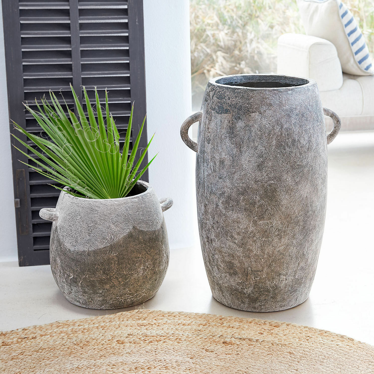 Set de 2 macetas Cœuron Dos macetas de hormigón gris de diferentes tamaños con asas, una con hoja verde, decoración interior