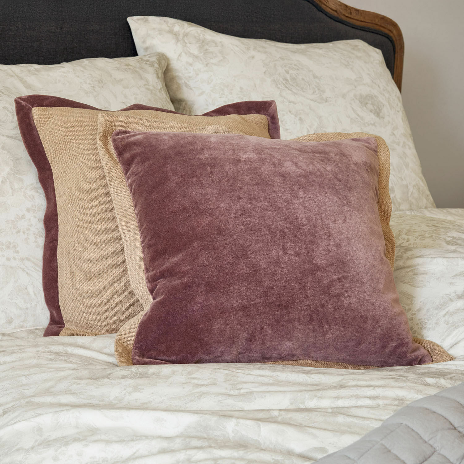 Set de 2 fundas de cojín Liréan Conjunto de cojines decorativos de terciopelo y lino en rosa y beige sobre cama con ropa de cama floral