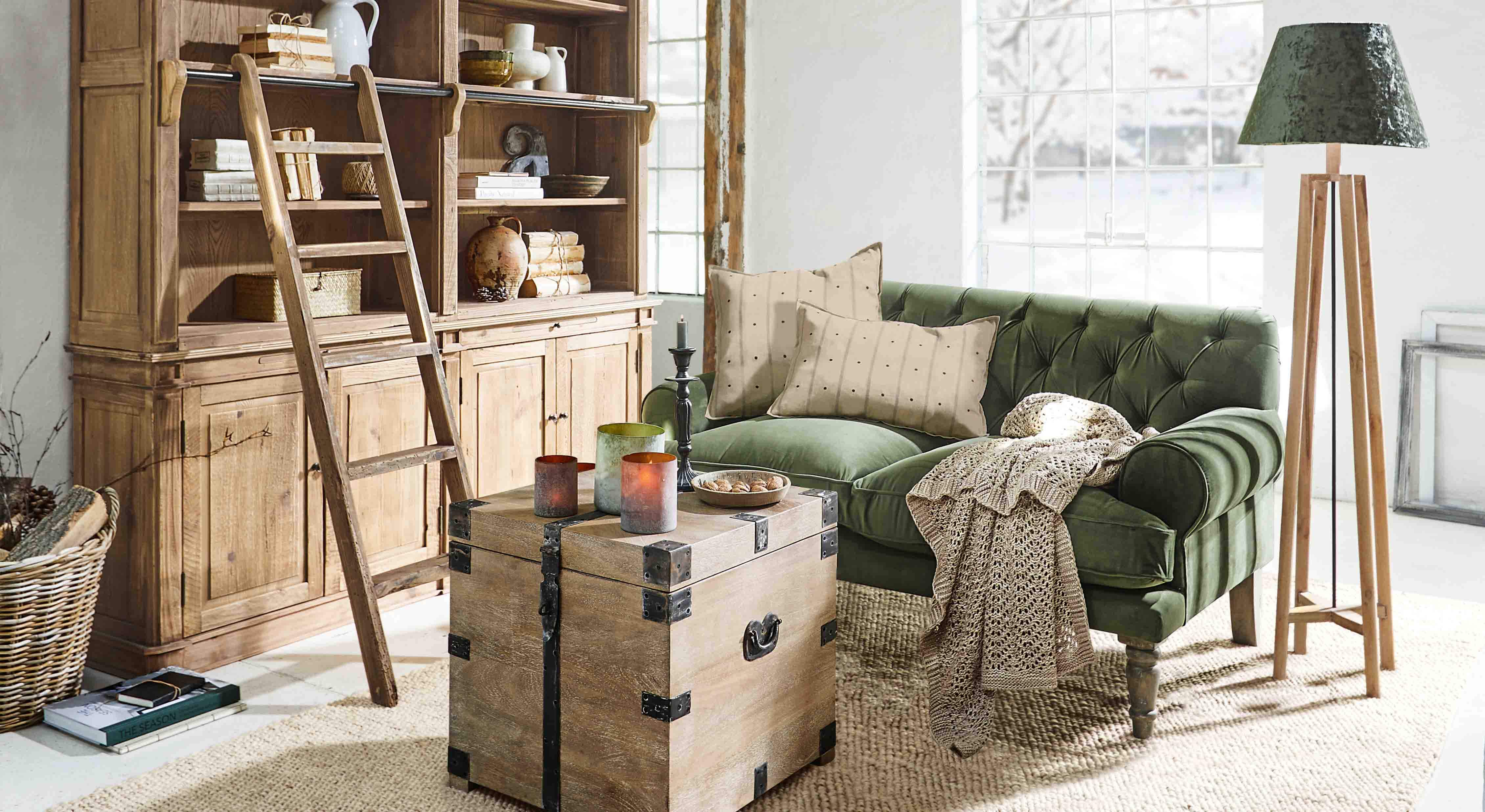 Salón acogedor con sofá verde de terciopelo, armario de madera y lámpara de pie de madera natural