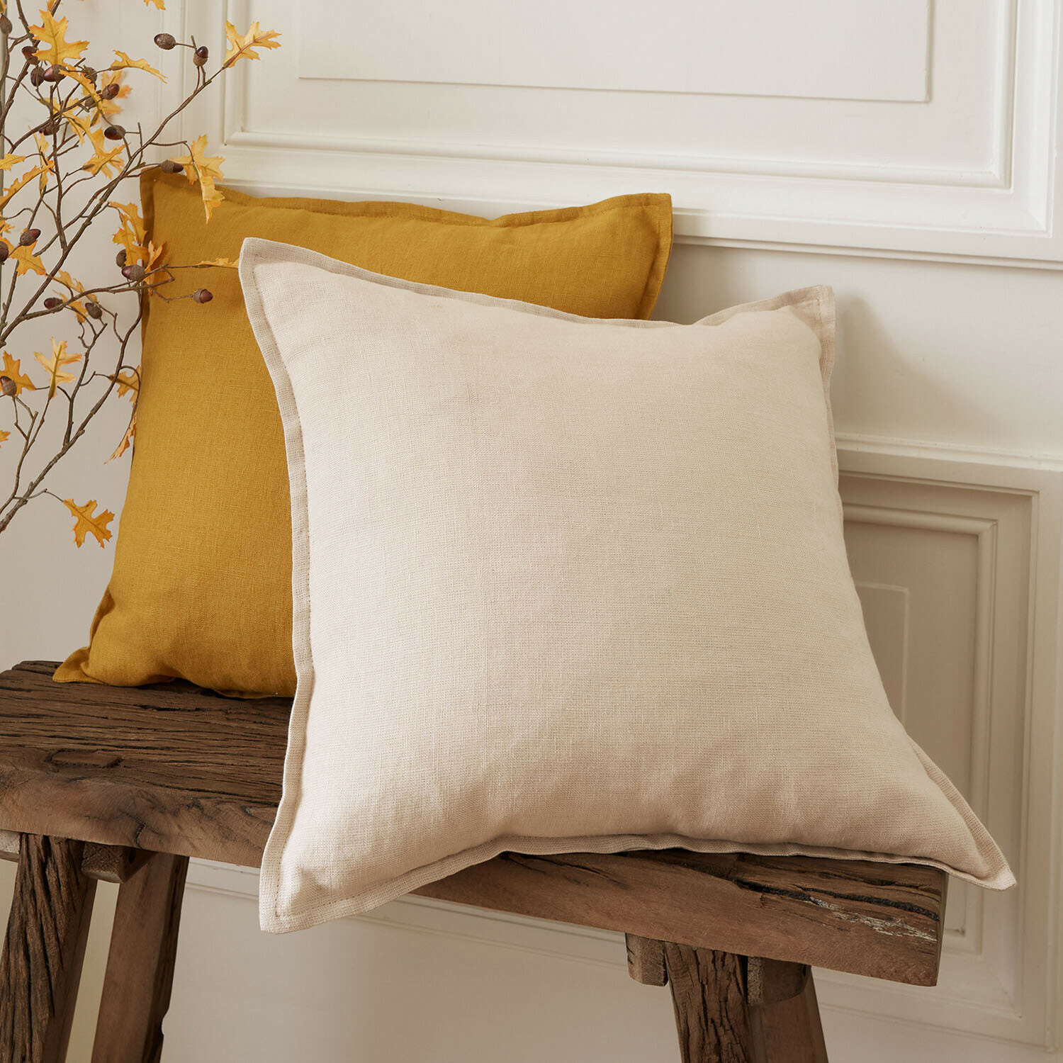 Set de 2 fundas de cojín Orsavine Dos cojines decorativos de lino en beige y mostaza sobre un banco de madera rústica